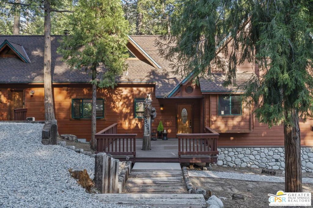 Lodge-style mountain cabin on Strawberry Creek, positioned close to downtown Idyllwild with dining and galleries nearby. Built in 2006 by one of Idyllwild's most respected contractors and offered for the first time, this 4 bedroom, 3 bathroom home spans 2,332 sq ft and features central heating and air, high-quality finishes, and a prime creekside location.Soaring ceilings with massive exposed beams give the living room its mountain lodge character. A stone fireplace anchors the space, while large picture windows capture the forest and sliding doors open to a wide deck where the sound of the creek carries through the trees.The kitchen connects directly to the living area with granite counters, generous workspace, and a long bar with seating that keeps the cook engaged with guests. Ample cabinetry, high-quality finishes, and a cooktop range make it well equipped for both everyday cooking and entertaining.The north wing is dedicated to the primary suite with a large shower, soaking tub, walk-in closet, and a sitting room with a built-in vanity. A loft above offers flexible use for reading, work, or guests.The south wing has a split-level layout. Upstairs are two guest bedrooms, one with its own bathroom and private deck with wooded views. A lofted space on this level works well as a playroom or sleeping area. The lower level includes a utility and laundry room with backyard access, another bathroom, and a guest bedroom with a walk-in closet. The backyard reaches the creek, where a natural sitting area offers a quiet place to gather under the trees with the sound of water all around.This custom mountain home combines thoughtful design, quality construction, and a location that captures the best of Idyllwild living.