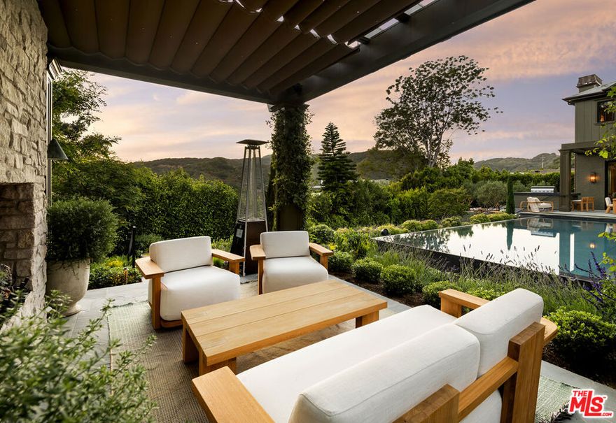 Perfectly situated in the coveted Pacific Palisades Riviera and set behind gates amidst lush and spectacular landscaping is this remarkable estate. The flawlessly executed interiors created by the renowned interior design firm Pierce and Ward, along with the home being a newly built Ken Ungar estate, make this home truly-one-of-a-kind. Every inch of the home, inside and outside, has been transformed to capture the striking canyon views and beams of light glowing through soaring windows and doors from sunrise to sunset at carefully designed vistas throughout the day. Enter through a stunning glass door to ultra-inviting living and dining rooms designed for daily enjoyment, with lavish yet welcoming interiors that appeal to all, featuring a London-chic flair mixed with mid-century design that will surely rival the best home designs executed in all of Los Angeles. The super-inviting family kitchen, with double banquet nooks you won't want to leave all day, offers counter seating, a top-of-the-line Wolf range, multiple ovens, double sinks, and wall-to-wall refrigeration, all opening to a large, stunning family room reminiscent of a chic boutique hotel. This space seamlessly transitions to a large outdoor dining table and chef's barbecue area, ideal for cooking and entertaining guests, all with stunning canyon views. The first floor also features a tucked-away office and a spacious downstairs suite, all carefully laid out with the architect's clear understanding of a masterful floor plan. The second floor boasts a primary suite tucked in its own wing, with dual doors, a fireplace, two walk-in closets: one on each end, a luxurious bath suite, for two, with an oversized double shower, soaking tub, two water closets, separate sink areas, and make-up seating for her, all with beautiful views of the meticulously landscaped grounds and a balcony completing this truly intimate and cozy suite. Across the landing, the second floor also offers a cozy upstairs family room set between three suites, each designed with extraordinary interiors and beautiful tree-top views. An elevator services all three floors, including the lower level, which features the single most inviting screening room, clearly designed for family and friends' movie nights. The lower floor also boasts a large open family room/pool and game room, a stunning bar area, and a wine room, all opening to a cozy patio with plenty of room to enjoy a cold plunge after Pilates in the custom-designed double studio suite and sauna. Down the hall, there is a jaw-dropping four-bed bunk room suite, perfect for late-night sleepovers or additional holiday guests. To complete this lush estate, there is an infinity-edge pool, oversized Baja shelves and spa, a built-in trellis with a fireplace, and a lower-level multiple seating area for guests, parties, and late-night conversations in this award-worthy landscape design encasing the entire estate. Simply exquisite and clearly one of Pierce and Ward's finest design and landscape visions.