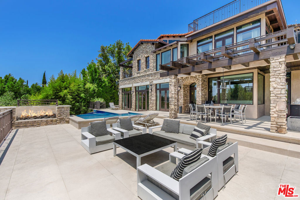 Experience a life of impeccable style and supreme comfort at this expansive, move-in-ready estate designed for the modern entertainer, with a variety of terraces, lounging areas, and outdoor spaces that harmonize with the home's natural surround and dramatic vistas. It enjoys a unique position immediately neighboring celebrity-rich Beverly Park's 24-7 guard-gate, with its around-the-clock patrol, and overlooks the exclusive community's mansion-studded grounds. The home's organic cobblestone facade is complemented by bold, sharp lines, resulting in a fusion of classic and contemporary architecture. Enter the elegant foyer to discover a totally done layout with everything included. In the step-down living room, bursts of greenery appear through arched windows flanking the river-rock fireplace. Exposed beams overhead repeat into the formal dining room as a bank of French doors open to the outside. The gourmand's kitchen features an oversized island, farm and prep sinks, garden window, an abundance of cabinetry, beautiful stone backsplash, recipe desk, and chef-grade appliances including Wolf range with hood and pot filler. In the family room, floor-to-ceiling paned windows frame gorgeous rolling hills and mountains. Upstairs, the primary suite has its own private balcony plus lavish spa-inspired bath with jetted marble tub, separate oversized shower, and dual-sink vanity. A large walk-in closet has built-ins and dresser island. A wraparound terrace with fireplace can be accessed by primary and secondary bedrooms, perfect for evening conversation fireside. Other amenities include an elevator, large media/gaming room, massage area with steam room, wine cellar, and gated driveway leading to a massive finished ~2,172-square-foot eight-car garage, an auto enthusiast's dream! Facing breathtaking views, the rear grounds include an infinity pool and spa, baja shelf, multiple gathering and lounging patios, and outdoor dining room with barbecue for dining al-fresco. Ascend the Tuscan spire to the top-most-level and behold 360-degree vistas from the sprawling rooftop deck. Relish this fresh, private lifestyle just moments to Sunset Boulevard, The Beverly Hills Hotel, the fine dining and shopping of Beverly Hills, and all the Westside has to offer.