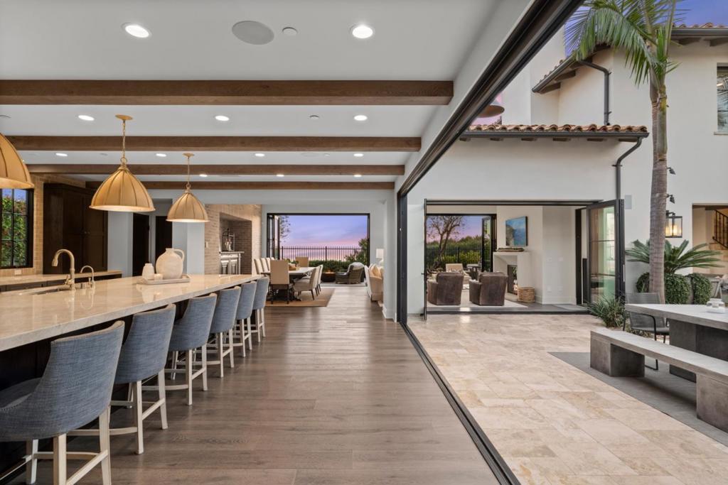 Nestled within the prestigious guard-gated enclave of Crystal Cove, this exquisite 5,300 sqft estate blends coastal elegance with modern sophistication. A grand entry, framed by koi ponds & cascading water features, sets the stage for this serene retreat. Designed for seamless indoor-outdoor living, retractable doors connect the great room & gourmet kitchen to multiple entertaining spaces. A custom outdoor kitchen, oversized spa, and lush landscaping create a private coastal oasis. The chefs kitchen boasts an oversized island, Wolf & Sub-Zero appliances, a spacious butlers kitchen, and ample storage. Wood-beamed ceilings, wide-plank French Oak floors, and marble & quartzite countertops add timeless charm. Smart home features include Savant automation, SONOS sound & solar panels. The main-level primary suite offers a spa-inspired haven, while two upstairs guest suites and a versatile bonus room provide additional comfort. A private guest casita within the gated courtyard serves as an exclusive retreat. Above the loggia, a separate office boasts a secluded workspace. Residents enjoy access to the Canyon Clubs pool, fitness center & sports courts, while Crystal Cove Promenades upscale dining, shopping & the beach are just moments away. Experience the pinnacle of coastal luxury.