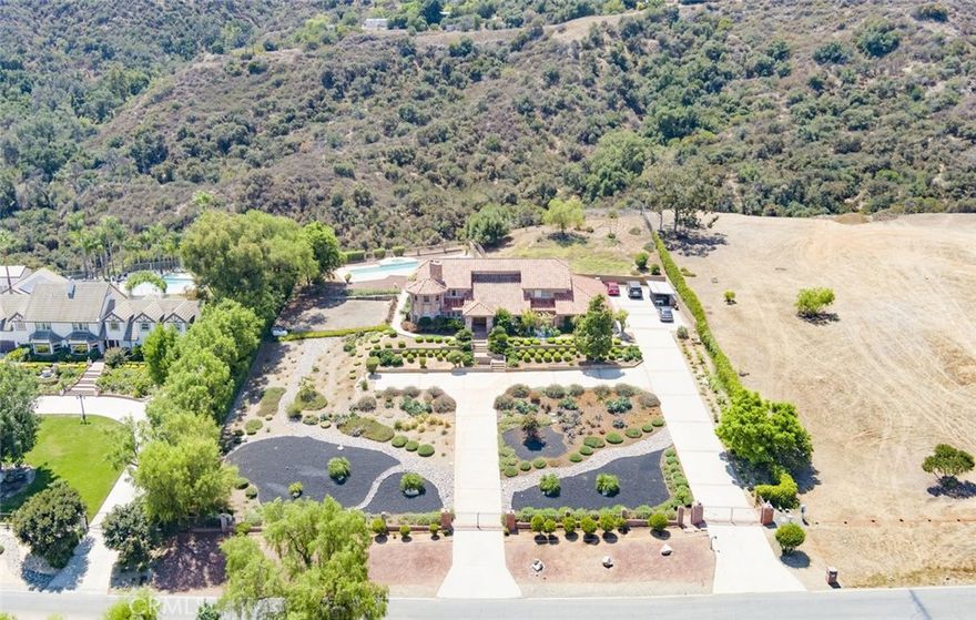Welcome home to this 5-acre estate located on the exclusive hillside of South Corona adjacent to the expansive beauty of the Cleveland National Forest. This 5,000 sft Spanish influenced home is has a sweeping views of natural hills and city lights.  Terracotta brick flooring to the hardwood French sliding doors and vaulted pinewood ceilings. Double door entry into the spacious foyer, with stark white arched doorways and contrasting hardwood trim.  This home is ideal for entertaining both sizable events and intimate family gatherings.  The family room has a dual fireplace that is shared with a cozy sitting room with views of the city below.  The kitchen flows into the game room with walk-behind wet bar and vaulted paneled ceilings. The

lower level features an ensuite, walk-in closet and quaint private brick patio where you can sip morning coffee and enjoy the gorgeous view. The grand staircase ascends to the upper level with 4 additional bedrooms and 3 bathrooms, which include an ensuite and the primary suite. The primary retreat is a private haven featuring a fireplace and sitting area. The spa-like bathroom has a marble soaking tub, walk-in shower and expansive walk-in closet with custom built-ins. If tranquility is what you desire the adjacent meditation room is an ideal retreat to escape into a good book or a quiet conversation.  Outside there is a pool and spa with the deck overlooking the incredible South Corona landscape and incredible sunsets. Enjoy the convenience of a 4-car garage and RV parking. There is even an existing level area for a future sport court or additional unit. Embrace this opportunity to make this exceptional property your Southern California sanctuary.