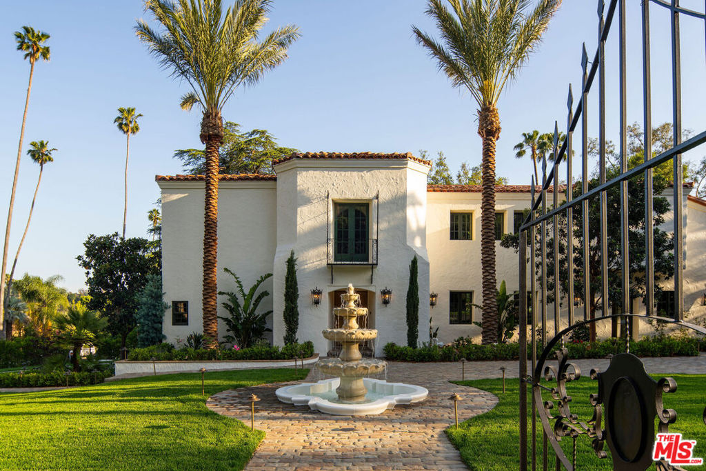 Perched along Eagle Rock's illustrious Hill Drive, The Gatsby is a rare and remarkable offering, rich in pedigree, privacy, and timeless elegance. Originally built in the 1930s and reimagined by legendary architect Paul R. Williams, AIA, this storied estate has been lovingly restored by Gary Mkrtichyan of Opus Builders, blending old-world craftsmanship with modern-day refinement in perfect harmony. From the exterior, The Gatsby evokes the romantic grandeur of Spanish Colonial Revival architecture, with graceful archways, ornate wrought ironwork, hand-carved wood details, vibrant tilework, terracotta rooflines, and lush, manicured gardens spread across nearly three-quarters of an acre. A stately four-tiered fountain greets you upon arrival, guiding you to a beautifully restored wood door that hints at the magic within. Inside, a soaring vaulted ceiling with hand-stenciled wood panels and exposed beams immediately captures the eye, a breathtaking tribute to Paul R. Williams' signature artistry, an exquisite blend of architectural poetry and old Hollywood glamour. The generous living room unfolds into a stunning kitchen and formal dining room, designed for both intimate dinners and grand celebrations. At the heart of the kitchen is an oversized center island overlooking a dramatic 12-burner La Cornue range. Custom cabinetry, a wood-paneled refrigerator, built-in wine fridge, and a secret walk-in pantry elevate the space with effortless grace and functionality. French bi-fold doors reveal a resort-style backyard where romance lingers in every detail, from the herringbone-tiled pool and spa to the fire pit and winding garden paths that invite quiet reflection beneath the stars. Just beyond, a private sports court adds a playful, spirited contrast to the tranquility, while an expansive grassy lawn, multiple seating areas, and mature trees, including a majestic oak, offer a sense of serenity and space rarely found. Just off the main living area lies a quiet retreat: a formal study and adjoining office, wrapped in rich wood paneling that radiates warmth and sophistication. Magnificent chandeliers cast a golden glow over each room, while French doors reveal an enchanting rose garden that gently winds down to an enclosed greenhouse, a dreamy setting for sunlit lunches, afternoon tea, or moonlit cocktails. Upstairs, a staircase adorned with original tile and wrought iron detailing leads to the spectacular primary suite. Here, a fireplace adds warmth and charm, while French doors open to a wraparound balcony with sweeping views of the grounds. The luxurious bathroom, complete with dual showers and a gold-plated soaking tub, invites indulgence. Three additional bedrooms, two bathrooms, and a second laundry room with access to a private sundeck above the three-car garage complete the upper level. A guest bedroom and bath on the main floor provide comfort and privacy. On the lower level, a hidden treasure awaits. Known as The Velvet Room, this authentic Prohibition-era speakeasy seems to echo with stories from another time. With secret rooms, a built-in bar, a fireplace, and private access to the backyard, it's a moody and unforgettable escape, where the spirit of the Jazz Age still lingers in the air. From sun-drenched interiors to hidden corners of enchantment, The Gatsby is a home built not just to impress, but to inspire. With architectural legacy and emotional depth, this is more than a residence. It's a legend reborn. And for the first time in generations, its doors are opening.