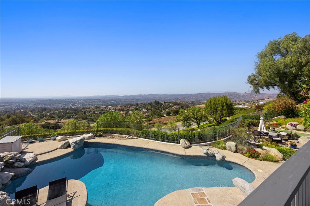 This home is a WOW in every sense of the word!!! A carpet of city lights is your backyard with breathtaking grounds that offer every amenity to make you feel like you are in a Polynesian resort. Custom designed sparkling pool with a dramatic rock waterfall, putting green, and a palapa-covered BBQ center for those very fun events. You are literally on top of the world to enjoy star gazing and watch the city come alive at night. On top of all that there is a separate garden with bountiful fruit trees including peach, avocado, and apple. Step inside to the soaring ceilings and expansive windows that flood the home with natural light, accentuating the richly stained wood and porcelain tile flooring throughout. The formal living and dining rooms, ideal for entertaining, open through French doors to the scenic outdoors. The chef’s kitchen is a culinary showpiece—outfitted with a center island, gleaming granite counters, a full tile backsplash, customized open shelving, top-tier appliances and generous walk-in pantry. A charming casual dining nook is set into a sunny bay window, while the adjacent family room features a warm fireplace flanked by custom built-ins and a full-size walk-behind wet bar with attractive copper ceiling. A versatile downstairs bedroom or office and a full bath offer flexibility for guests or workspace. Upstairs, the luxurious primary suite is situated at the rear of the property, and is a true retreat—complete with its own intimate fireplace and jaw-dropping view balcony, where you’ll savor the evening stars and blankets of distant lights. The spa-like bath boasts sleek tile flooring, rare gleaming Blue Ice granite countertops, dual sinks, separate vanity, large walk-in shower with custom tiles, and a sumptuous soaking tub set within a picturesque bay window which will surely invite you to linger a bit longer taking in the mesmerizing views. Three additional bedrooms round out the second level, including one with its own en-suite bath. Additional amenities include a spacious three-car garage with epoxy flooring, built-in storage, and gated RV parking. This stunning home situated on an intimate cul-de-sac that effortlessly combines elegance, comfort, and captivating views. Zoned for top ranked schools, minutes to great hiking and biking with Deer Canyon Park and Cleveland National Forest, nearby shopping, restaurants and Anaheim Hills Golf Club makes this the perfect house and location! You don't want to miss this one!
