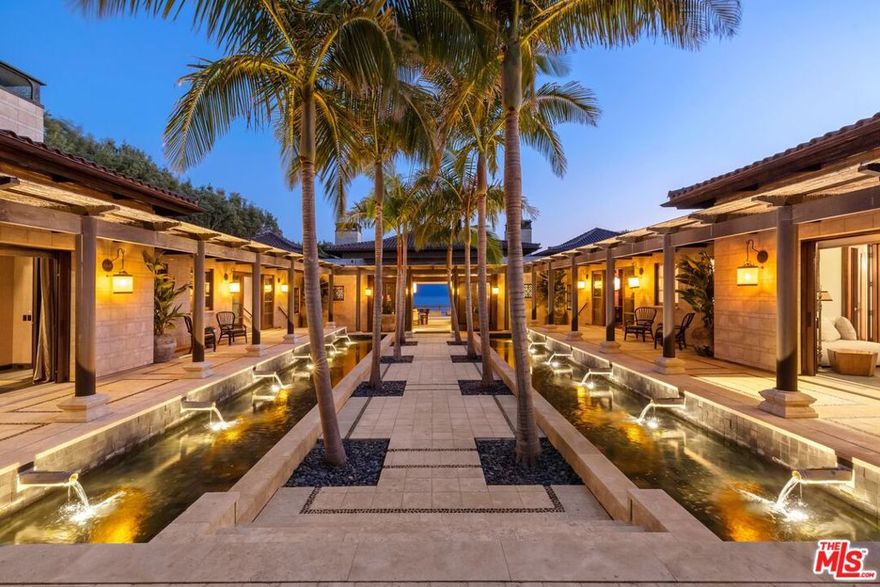 With breathtaking views, Bali-inspired design, and every contemporary comfort, this magnificent estate is a serene sanctuary for exquisite living and impressive entertaining. The private, gated property of over 1.2 acres extends from PCH to Malibu Road, perfectly landscaped and commanding expansive ocean views. A long palm-lined drive leads past a two-story, two-bedroom guesthouse, a lighted north-south tennis court and pavilion, and a fountain, waterfall, and gardens before arriving at the enormous motor court and four-car garage. A dramatic gateway and long, serene palm-lined reflecting pool lead between the wings of the U-shaped house to the gorgeous double-door entry. With interiors designed by Martyn Lawrence Bullard and stunning sight-lines to the ocean, the house is detailed with ornate wood carving, very tall beamed ceilings, wood and stone floors, and full-width exterior doors that vanish to offer seamless flow between indoors and out. The entry steps down to the formal living room, which includes a generous dining area, a pair of facing fireplaces, and a wall of glass that opens onto a roomy patio with a fireplace, stunning ocean view, and a nearby fountain and barbecue island. Adjoining the living room is a spectacular ocean-view great room that includes a family room with fireplace, dining area, and a gourmet kitchen with a huge stone-topped island with seating, deeply recessed tray ceilings, beautiful cabinetry, and a pantry. One wing of the house has two bedrooms and a laundry room. The other wing features a majestic ocean-view owner's retreat with high wood beamed ceilings, beautiful wall coverings, wood floors, and a wide glass doorway opening to a tranquil covered patio. A hallway leads to a luxurious bath, two very large closets/dressing areas, and, at the end of the hall, a resplendent Bali-inspired library/study with high coved ceilings, a wall of built-in book shelves and cabinets, a fireplace, and doors to the patio and to a private sitting area. The home's lower level features a party-perfect bar room highlighted with ornate metalwork that encloses a large wine storage area. The bar extends into a spacious tiered home projection theater. A long hallway leads to a second powder room, a changing room, and another bar, which opens to the lower patio, spa, sitting areas, and lawns, as well as the infinity ozone pool, patio, cabana, and private steps to Malibu Road and access to the beach/ocean. With Crestron electronics and full-house water filtration, this remarkable estate is a livable legacy.