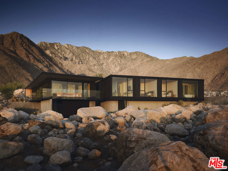 This home represents a fresh take on Palm Springs modernism, blending mid-century inspiration with contemporary design. Featured in Robb Report, Wallpaper Magazine, Dwell, and Palm Springs Life, it has received international recognition for its architectural significance. Located in the guard-gated community of Desert Palisades, the 4-bedroom, 4.5-bath residence is designed to capture expansive desert and mountain views through walls of glass. Influenced by Japanese Wabi Sabi principles, the interiors highlight natural textures and refined materials, including Hemlock wood ceilings, Calacatta and Taj Mahal stone, French oak, and limestone. The exterior, clad in charred shou sugi ban, offers a bold architectural presence against the landscape. Inside, the primary suite features panoramic views, a spa-inspired bath, and a custom walk-in closet. Each additional en-suite bedroom is individually designed, while amenities such as a dedicated gym, elevator, and seamless indoor-outdoor flow enhance comfort and convenience. Outdoor spaces include an infinity-edge pool, fire feature, built-in BBQ, and multiple lounge areas, creating an ideal setting for both entertaining and everyday relaxation. Designed by architect Jill Lewis, this home balances modern architecture with the surrounding desert environment. An adjacent half-acre parcel, with approved plans for a 5,100-sq-ft residence, is also available--offering the option to expand or create a second home.