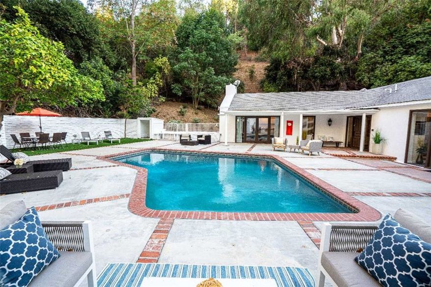 Sitting on nearly half an acre, this updated villa nestled in the heart of Studio City is a MUST-SEE to truly appreciate. Set back more than 125 feet from the street, you enter the estate through a generous motor court and over a bridged stream with parking for more than 10 cars. The entry is surrounded by luscious trees, abundant gardens, and lush nature yards. The foyer opens into the formal living room and dining room with views overlooking the vast pool. The vaulted and beamed ceilings enhance the warmth of the living, family, and dining area which is accentuated by natural light. The well-appointed kitchen has a Viking range and enormous prep island with bar sitting. The master bath has an infinity entry shower and all rooms open to the serene hillside. Abundant patios for indoor-outdoor dining provide endless entertaining opportunities.  A separate guest house opens to the pool courtyard.  Large lot invites adding extensive square footage and personal touches. This is a one-of-a-kind private and serene home awaiting that discerning owner desiring a majestic gem in their own enchanted forest.