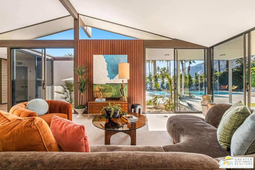 Designed in 1969 by Hugh Kaptur, AIA, and thoughtfully restored in 2025 with his blessing, this exceptional single-level post-and-beam residence reflects the architectural clarity and restraint that define Kaptur's most enduring work. Located on an ultra-private cul-de-sac in the heart of Movie Colony, the home honors its pedigree while presenting with renewed integrity. Clean lines, open-plan interiors, and rhythmic colonnades establish a strong architectural framework, while expansive walls of floor-to-ceiling glass and sliding doors dissolve the boundary between indoors and out. Mountain views unfold to the west, with nearly every room opening directly to the landscape. The light-filled living room is a signature moment defined by vaulted, exposed-beam ceilings, warm wood-paneled walls, integrated built-ins, and a substantial fireplace anchoring the space. Clerestory windows and a serene interior atrium further enhance this area's connection to light and nature. The adjacent kitchen is crowned by floating light panels and features Walnut cabinetry, stone countertops, Fisher & Paykel appliance suite, and a pass-through to the dining area reinforcing the home's original modernist flow. All primary living spaces extend to a covered patio overlooking the ultra-private south and west-facing backyard, where Mount San Jacinto views frame a pool and spa, open-air fireplace, and generous lawn creating an elegant extension of the architecture itself. The west-facing Primary Ensuite opens directly outdoors and includes dual sinks, a south-facing walk-in shower with views, and a custom walk-in closet. Junior Ensuite Two opens to the front courtyard and enjoys a private bath with walk-in shower. Bedroom Three offers pool and mountain views, while a hallway powder bath serves guests. Just moments from downtown Palm Springs, this is a rare opportunity to own an authentic, architect-restored Kaptur residence in one of the city's most cherished neighborhoods. Ideal for full or seasonal enjoyment as well as those seeking a prominent short-term vacation rental.