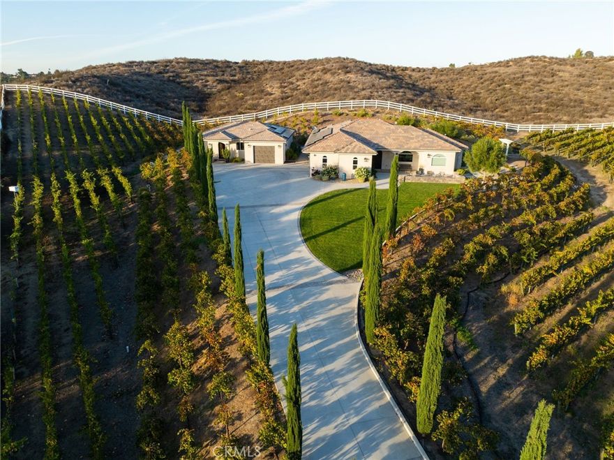 Crafted with a keen eye for detail, this newer-construction custom estate combines high-end finishes, quality craftsmanship, and clean modern lines with a warm, practical feel—all set on 2.5 usable acres in the heart of Temecula’s sought-after Wine Country. The property features a 3-bedroom, 2-bath main residence and a separate 2-bedroom, 1.5-bath guest house, both showcasing a cohesive contemporary design with a smooth Santa Barbara-style stucco exterior finish for a clean, upscale look. Inside the main home, an open-concept layout creates effortless flow between the living, dining, and kitchen areas—ideal for entertaining and everyday living. The designer gourmet kitchen offers high-end finishes, a large center island, and  generous storage, all styled with a refined, modern aesthetic. Thoughtful interior design details continue throughout, with curated fixtures, quality materials, and elevated yet comfortable spaces that feel polished without being sterile. The separate guest house includes 2 bedrooms, 1 bathroom, and a full kitchen, making it perfect for multi-generational living, extended stays, or additional income opportunities as an owner-hosted short-term rental in this popular Wine Country destination (buyer to verify STR requirements).Recently installed solar (2025) with Tesla Powerwall enhances efficiency and energy independence. The fully fenced property with privacy gate includes approximately 2.5 acres of land with an organic, income-producing vineyard of mature, healthy vines—ideal for an aspiring or seasoned vintner. For those who simply love the ambiance of the vines without the upkeep, the vineyard can be professionally managed and harvested by a third party, allowing the owner to enjoy the beauty and lifestyle of Wine Country without the maintenance. Temecula Wine Country living at its finest—modern design, custom construction, income potential, and a turnkey vineyard experience all in one exceptional estate.