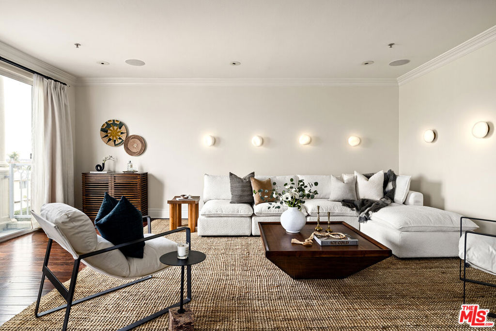 Unit 301 boasts an enviable layout, the most spacious of this charming building's six condo homes. Two sets of sliding glass doors frame the fireplace and open onto a pair of eastward-facing balconies that fill the open living-dining area with natural light. You can catch glimpses of the Hollywood skyline, including the Griffith Observatory, from your sofa, dining table, and private patio. The guest bedroom includes a built-in workspace and could easily double as your home office. The en-suite primary bedroom includes a generous walk-through closet that leads to a chic oversized bath with a free-standing soaking tub, new tile floors, new marble shower tile, a new shower, and new sink & light fixtures. If you run out of room in the primary closet, fret not: a custom shoe and accessories closet has been added to the end of the hallway to keep your finds well-organized. The guest bathroom has been shown an equal amount of style and care, with a remodeled step-in shower with marble tile and upgraded fixtures. Unit 301 has been extensively updated, including new limestone tile floors and quartz countertops in the kitchen, new hardware, fixtures, and fresh paint throughout, and an integrated sound system. Statement lights in the primary bedroom and dining area bring a bit of panache, but the designer pebble light sconces lining the living room walls help make this home feel truly unique. 1023 Wilcox Ave is located in the heart of the Hollywood Media District; this central location gives you quick and easy access to some of the best dining in the city, including Providence, Mother Wolf, and Rao's. It's also just down the street from Gold's Gym and movie nights at Hollywood Forever Cemetery. Melrose and Larchmont Village are close enough that you can leave your car at home in one of your two spaces in the gated, subterranean lot.