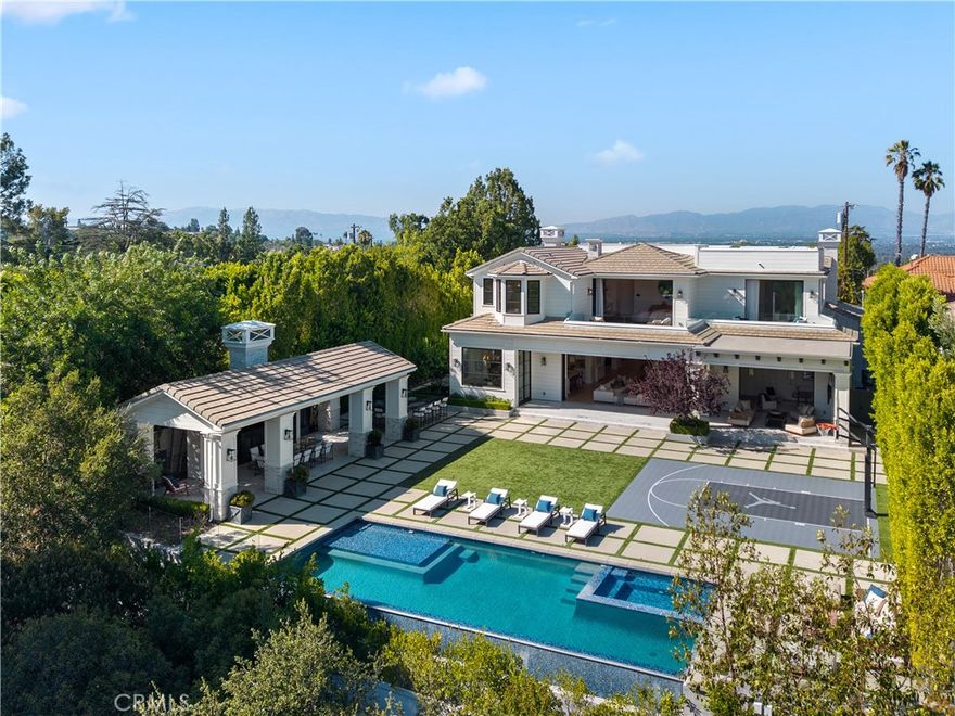 Tucked away in the hills of Encino on a peaceful cul-de-sac, this architectural tour de force effortlessly combines timeless elegance with modern luxury and sweeping panoramic views. Behind grand double doors, an impressive foyer welcomes you with soaring ceilings and a dramatic spiral staircase, setting the tone for the home's sophistication and scale. The expansive open-concept main level is designed for both lavish entertaining and comfortable daily living, featuring a seamless formal living and dining area, a stylish family room with a sleek bar, a temperature-controlled wine cellar and dual pocket glass doors that open at the touch of a button offering a true indoor-outdoor lifestyle. At the heart of the home is a gourmet chef’s kitchen, outfitted with top-of-the-line appliances, double islands, a sunlit breakfast nook and a well-appointed butler’s pantry. Upstairs, you’ll find three ensuite bedrooms and an opulent primary suite complete with dual spa-like bathrooms, a custom walk-in wardrobe and a pocket glass door opening to a large private balcony overlooking the backyard oasis. The lower level is designed for pure indulgence, featuring a glass-enclosed office, billiards lounge, plush home theater, serene massage room with a sauna and an additional patio with direct access to the backyard. Surrounded by mature hedges for added privacy, the resort-style backyard offers a sparkling infinity-edge pool with a large spa and baja shelf, a 600 sq ft cabana, an outdoor kitchen with bar seating and a sports court. Crowning the estate is a showstopping 1,000+ sf rooftop deck with commanding views of the Valley perfect for sunset cocktails or stargazing. Additional features include two main-level ensuite bedrooms, dual laundry rooms, mudroom, elevator, soaring ceilings, Control4 smart home automation, a gated driveway and a three-car garage. Ideally located south of the Boulevard within the coveted Lanai Road School District and just minutes from the Westside, the Valley and world-class amenities.