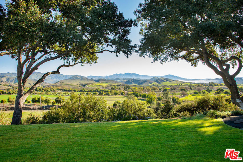 Unparalleled beauty and style define this reimagined ranch estate, offering breathtaking views of the entire Santa Ynez Valley and the surrounding mountains. A level of design sophistication rarely seen in the Valley has been seamlessly integrated into the recent rebuild of this 1965 mid-century masterpiece. Set back on a flat, elevated 6.33-acre private mesa in the prestigious Rancho Estates, near the intersection of Baseline and Happy Canyon Road, the property provides sweeping vistas of the horse ranches and wineries below. Century-old oak trees frame the landscape, while expansive lawns and meadows surround the residences. As you approach the main residence via the olive tree-lined drive, passing a two-acre pasture, you arrive at the massive steel-framed entrance door. Inside, your gaze is immediately drawn to the soaring, raw cedar-lined architectural ceilings and, beyond, through walls of glass, to the towering oak trees, the pastoral valley, and the Los Padres Forest that frames the entire vista. In addition to the main ranch house, the property boasts a guest house/gym/office structure, a workshop, chicken coops, and a bee house. The owner also has plans for an entertaining barn. The orchard is abundant with apple, pear, fig, apricot, plum, and peach trees, as well as raspberry and blackberry bushes, and champagne grapevines. The harvested olives recently yielded 4 tons of fruit, which provided a 55-gallon barrel of organic pure EVOO at the Figaro Farms press. The circular pool and spa, designed to resemble an artistic pond, operate on an AOP system (a combination of UV and ozone for minimal chlorine usage). Relax and enjoy the views from one of the many thoughtfully curated outdoor spaces, including the vista-point fire pit area. Additionally, the upper yard is completely fenced in. Uniquely for this region, the property is equipped with its own private, dedicated fiber optic line, not shared with any other properties. This invaluable asset ensures seamless streaming, podcasting, and business operations. The design elements throughout the home are nothing short of breathtaking, featuring brass, copper, and raked concrete finishes, an Italian marble bar, wine storage, multiple fireplaces, and a gourmet kitchen outfitted with Wolf and Miele appliances. Smart home upgrades throughout the main house, guest house, gym, and outdoors include lights, sound systems, and security integrated on Control4. All of this is just a short distance from Santa Barbara, offering a rare blend of seclusion and accessibility. Come experience an unrivaled lifestyle of luxurious design in a stunning pastoral setting. We can confidently say that you haven't seen anything like this in the Santa Ynez Valley.