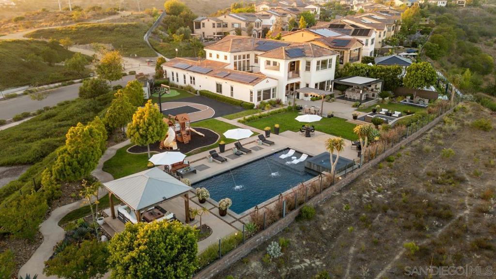 ** Value Range Priced $4,299,000 - $4,399,000** A rare offering of sophistication, scale, and serenity—this showstopping residence is one of Del Sur’s most iconic homes. Privately nestled on an all-usable, half-acre view lot, and masterfully reimagined by a professional interior designer with nearly $1M in custom upgrades, the home blends curated luxury with everyday livability. Beyond the statement-making entry—soaring two stories and centered by a crystal-drum chandelier—every space tells a story. The kitchen is a true centerpiece, anchored by a dramatic Belvedere quartzite island with waterfall edge, mirrored metallic backsplash imported from Spain, Tom Dixon pendants, thoughtfully placed accent lighting, and custom cabinetry with smoked-glass uppers. A full suite of KitchenAid appliances, butler’s pantry, and walk-in pantry make the space as functional as it is fashionable. The dining room stuns with a tiled accent wall, wood-paneled ceiling, and impressive chandelier, while the family room is wrapped in windows and custom drapery, seamlessly connecting to the outdoor spaces beyond. The main-level primary suite is a retreat in itself, featuring dual custom closets, designer lighting, and a spa-inspired bath clad in marble with dual vanities, soaking tub, and walk-in shower. Upstairs, three additional ensuite bedrooms feature custom wainscoting, walk-in closets, and timeless finishes—alongside a large bonus room with balcony and easterly views. The crown jewel is the luxury resort-like backyard: oversized 20x40 pool with Baja shelf and water features, four-sided vanishing edge oversized spa, putting green, basketball half-court, California Room with fireplace and TV, sandbox, play structure, and multiple dining and lounging zones. An outdoor kitchen with refrigeration and 8-burner BBQ sits under a sleek custom pergola with motorized slats for sun or shade. Every inch is artfully framed by mature landscaping and canyon views with total privacy. A private-entry casita with its own living space, separate AC zone, kitchenette, walk-in closet, and full bath offers flexibility for guests, multigenerational living, or a chic studio space. Additional features include: European white oak flooring, custom millwork throughout, crown molding, motorized blinds, epoxy garage with built-in cabinetry, Ring camera system, dual tankless water heaters, and 22-panel paid solar system. Located in the highly sought-after Del Sur community with 11 pools, 14 parks, and top-tier schools. This is not just a home—it’s a lifestyle statement.