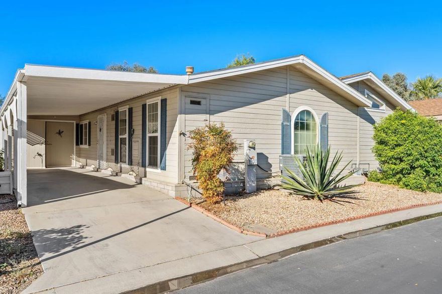 Discover this manufactured home on a permanent foundation, nestled in the prestigious Coronado Gardens community. Enjoy resort-style living with walking paths, a spacious clubhouse, pool and spa, sports court and putting green. This home features a large, covered patio perfect for relaxing. Step inside to a bright, open formal living area with a cozy fireplace and a sliding door leading out to the patio, creating the perfect retreat. The family room has abundant windows and seamlessly connected to the formal dining room. The kitchen features a brand new dishwasher, tile countertops, a pantry with pull-out cabinets, and a large window over the sink. With two generous bedrooms, including a master suite with ample closet space, a dressing area, and a separate tub and shower. An additional office/bonus room has been added and provides flexibility for work or hobbies.Additional highlights include a carport that easily accommodates two vehicles and an oversized workshop with plenty of shelving for storage or projects. This property is located close to shopping, hospitals, and more. Don't miss your chance to experience the best of 55+ living in Coronado Gardens.