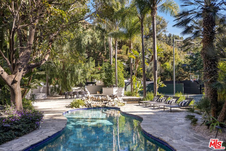 Set on a sprawling lot, this secluded Spanish Revival estate captures the allure of Old Hollywood with its harmonious blend of classic architecture and refined, warm living spaces. Tucked far back from the street behind a gated entry for complete privacy, the residence features a spacious motor court anchored by a majestic olive tree, offering a stately welcome to this remarkable sanctuary. Inside, a double-height entry foyer leads to a formal living room with a vintage fireplace and French doors that flood the space with natural light while seamlessly connecting to the lush outdoors. The estate's architectural details include tall, arched windows, intricate stained glass accents, and wrought iron embellishments, complemented by rich terra cotta elements and warm, dark woods. A chef-caliber kitchen flows effortlessly into a formal dining area, where French doors open to one of the home's many garden patios. Adjacent to the dining area is a timeless bar and game room, complete with a pool table, that extends to a private outdoor lounge and a covered dining areaideal for hosting and entertaining. The primary suite is a serene retreat, featuring vaulted ceilings, a cozy sitting area with a fireplace, and expansive windows framing picturesque views. Its spa-like ensuite bathroom is appointed with a dual vanity, rainfall shower, and indulgent soaking tub. Generously sized guest bedrooms provide comfort and privacy for family or visitors. Outdoors, the property transforms into a recreational haven. A full tennis and basketball court, sparkling pool, and jacuzzi are surrounded by lush tropical greenery, while a barrel sauna and cold plunge deliver the ultimate in relaxation. The outdoor kitchen and barbecue area, along with multiple alfresco and covered dining spaces, create endless opportunities for entertaining and embody true California luxury living. A hillside deck, perfect for stargazing, completes the exceptional backyard experience. Situated in a prime location in the Hollywood Hills, this residence offers easy access to the vibrant Sunset Strip while maintaining an air of tranquility. A masterpiece of privacy, elegance, and modern convenience, this property is a rare find, seamlessly blending the timeless charm of Spanish and Mediterranean architecture reminiscent of Old Hollywood with all the amenities of contemporary living