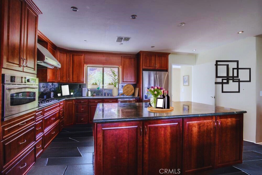 This stunning ranch-style home sits on 24 acres of agriculturally zoned land in Aguanga. The main residence features 4 bedrooms and 2 bathrooms, spanning 1,972 square feet of living space, with an additional detached casita that includes its own bathroom. Perched atop a hill, the home is surrounded by mature trees and offers sweeping views.
The kitchen is equipped with granite countertops, custom cabinetry, and upgraded stainless steel appliances, including an oven, separate convection oven, 5-burner cooktop, and a spacious center island. This open kitchen flows seamlessly into the living room, creating an ideal open floor plan. The living room offers large picture windows with scenic views and wooden ceilings with exposed beams. The bathrooms have been updated with modern countertops and upgraded cabinetry, and tile flooring is found throughout the home. The backyard includes a covered patio and an indoor laundry room, adding convenience and comfort.
The property boasts extensive usable land and is filled with potential, offering a unique opportunity to enjoy both comfort and the beauty of a vast, agriculturally rich landscape.