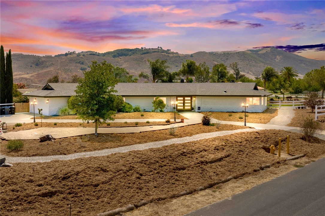 An exceptional opportunity to call the coveted Los Ranchitos community home. This architectural masterpiece has been completely rebuilt, blending refined modern design with extraordinary attention to detail. Set on 2.07 acres of flat, usable land, the home is gracefully framed by a circular driveway & manicured landscaping. Upon arrival, panoramic views of the De Luz hills set the tone for the timeless romance of this property. Grand, custom-crafted double wood doors welcome you inside, where natural light pours into open interior. Brand-new luxury vinyl plank flooring runs throughout, paired with all-new windows dressed in custom-fitted shades. The sunken living room exudes warmth, anchored by a wood-burning fireplace with striking detail, creating the perfect spot to curl up with a book, gather with friends, or simply unwind. Guests are welcomed with a thoughtfully placed half bath, while the formal dining area flows into the living room, making everything feel connected. Just steps away, the kitchen and family room share an inviting space that’s as practical as it is beautiful. With every detail carefully considered, the kitchen is a true centerpiece, equal parts showstopper and heart of the home, where sunlight highlights a custom tile backsplash, crisp white cabinetry, & rich brass accents. High-end appliances, including a wine fridge, complement the expansive quartz island, keeping the design both elevated & seamlessly connected. Beyond, the family room offers a comfortable gathering space framed by windows that draw the outdoors in, inviting easy conversation whether hosting friends or enjoying a quiet moment by the fire. Down the hall, tucked on the opposite side of the home, are four inviting bedrooms. Three generous sized rooms share an updated bathroom with dual sinks & a walk-in shower wrapped in green tile. The primary suite is perfectly scaled, with a bathroom that feels truly one-of-a-kind—an open-concept design blending a freestanding tub and walk-in shower, framed by dual sinks and beautiful finishes. A clean, modern laundry space adds both function and style. Outdoors, a barn with water and electricity awaits transformation, whether for horses, hobbies, or your own vision. Expansive open land offers endless possibilities. A resort-style pool and spa, heated by solar, sits nestled for exceptional privacy. Some places you simply have to feel to understand, this is one of them. Come see for yourself, & fall in love.