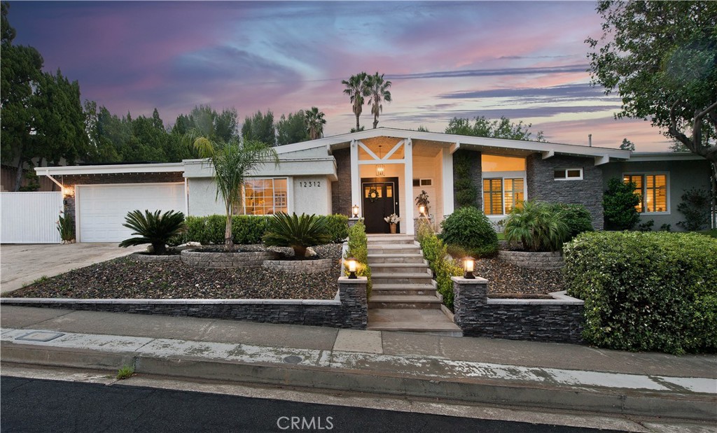 Welcome to this stunning single-story masterpiece with breathtaking golf course views, nestled in the highly sought-after Knollwood Country Club Estates of Granada Hills. Thoughtfully remodeled and upgraded, this entertainer’s oasis seamlessly blends Farmhouse and Coastal elegance, creating a serene and inviting ambiance. Step through the custom front door and into a light-filled, open-concept living space where French doors and abundant windows bathe the home in natural light. The grandeur of the vaulted ceilings is accentuated by double custom fireplaces, elegantly dividing the living and dining areas. The chef’s kitchen is both functional and stylish, featuring a center island with seating, double ovens, ample storage, and skylights that flood the space with sunshine. A versatile bonus area behind the kitchen offers the perfect setting for a home office, cozy family room, or tranquil morning retreat. With over 3,100 sq. ft. of living space, this home boasts an ideal four-bedroom layout. The impressive primary suite is a private sanctuary, complete with a fireplace, French doors, and sliding door access to the backyard, a spacious walk-in closet with built-ins, and a spa-inspired en-suite bathroom. Two additional bedrooms share this wing of the home, while a secluded fourth en-suite bedroom on the opposite end is perfect for multi-generational living, guests, or a home office. The 17,655 sq. ft. flat lot is an entertainer’s dream, backing onto the 16th hole of Knollwood Golf Course. Enjoy year-round outdoor living with a sparkling pool, oversized covered patio, built-in BBQ area, and a custom shuffleboard table that doubles as a serving station. Additional highlights include a motorized side gate for possible RV access, a storage shed, and low-maintenance artificial turf. Noteworthy upgrades include paid solar, upgraded electrical, newer insulation and ducting, new PEX repiping, a tankless water heater, and a custom indoor laundry room. This home is a rare find—a perfect blend of luxury, comfort, and functionality. Don’t miss the opportunity to make it yours!