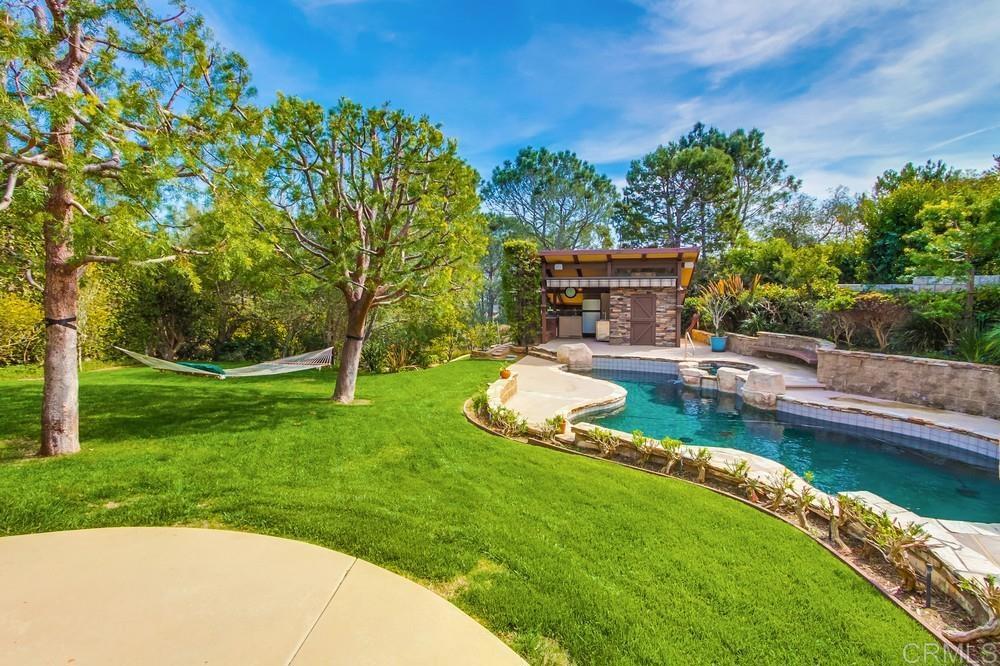 Located west of I-5 in the highly sought-after Olde Solana Beach neighborhood, this rare and expansive estate rests on a generous 28,700 sq. ft. lot. The property boasts stunning easterly views of sunrises and distant mountains, with charming peek-a-boo ocean views from the front. Step inside to discover soaring wood-beamed vaulted ceilings on the upper level, creating a warm and open ambiance. Thoughtfully remodeled in 2012, the home blends classic charm with modern sophistication. The gourmet island kitchen is a chef’s dream, featuring premium appliances and a cozy breakfast nook — the perfect spot to enjoy your morning coffee or tea. A formal dining room offers panoramic views across the estate, ideal for elegant entertaining. Both the kitchen and living room open seamlessly to multi-level decks equipped with retractable awnings and a built-in sound system, delivering the ultimate indoor-outdoor lifestyle. The main level includes a versatile bedroom or home office, while the lower level features a luxurious primary suite, two additional ensuite bedrooms, a bonus room, and an extraordinary wine cellar that holds up to 3,200 bottles. The cellar also includes a seating area and extra chilled storage, ideal for any wine enthusiast. Sustainability meets luxury with owned solar panels and a resort-style, solar-heated saltwater pool complete with boulders, a water slide, spa, and outdoor bar area with a pool bath. The beautifully landscaped grounds include meandering trails leading to a gazebo, walking bridge, greenhouse, and a ready-to-plant garden. Enjoy an abundance of fresh citrus from your own lemon, lime, orange, tangelo, and tangerine trees. Perfectly located near top-rated schools, Fletcher Cove Beach, Cardiff-by-the-Sea, the San Elijo Lagoon, shopping, dining, entertainment, and the train station — everything you need is within easy reach. With ample room for an ADU, sports court, or additional parking via a side driveway, this one-of-a-kind property offers space, privacy, and endless potential. Experience the best of coastal living — welcome to your forever home in Solana Beach.