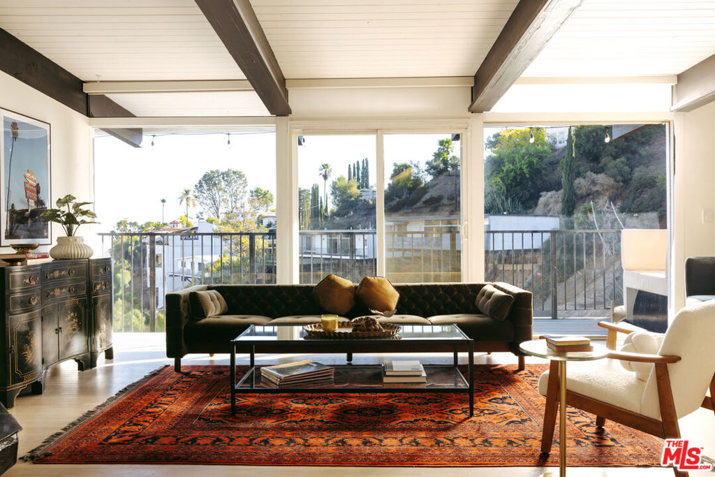 Perched among the winding roads of Beachwood Canyon, this 2-bed, 2-bath post-and-beam dream retreat is cinematic LA living at its best, beautifully balancing between vintage charm and modern elegance. Step through the iconic red double doors into a sun-drenched space where floor-to-ceiling glass frames breathtaking canyon and city views alike. Outside, a sixty-foot deck stretches the length of the home, turning sunset viewing into a nightly event. An ode to the golden era of Hollywood, the living space is anchored by a dramatic black lava-stone fireplace, surrounded by warm original hardwood floors, exposed beams, and abundant light. The open layout flows into a newly remodeled chef's kitchen with quartz countertops, custom cabinetry, stainless steel appliances, and an oversized island perfect for dinner parties, deep talks, or dirty martinis. The primary suite opens right onto the deck for coffee-at-dawn or wine-at-dusk moments. Both bathrooms are reimagined with floating vanities and modern finishes. Bonus points include a Level 2 Tesla charger, central HVAC, and an oversized steam shower. The second bedroom easily moonlights as a guest room, office, or podcast studio. Outside your door, this corner of Beachwood Canyon feels like its own little world, complete with a cafe, market, and post office. It's character, calm, and city-light magic with just enough wink and wonder to remind you why everyone falls in love with this town.