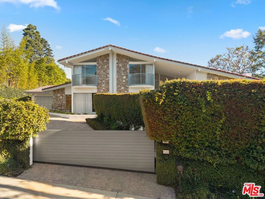 Set behind gates in desirable Brentwood, this bright and airy residence embodies the essence of California living. The spacious floor plan features four bedrooms plus an office, with seamless indoor-outdoor flow through expansive glass sliding doors. Designed for entertaining, the home offers two living rooms, a separate dining room, and a circular bar overlooking the pool and lush garden. The new kitchen opens to a sunny eat-in area, while soaring double-height ceilings in the foyer and a striking curved staircase add architectural drama. The private primary suite includes a sitting area with views of the city lights, creating a tranquil retreat. Outdoors, enjoy a large landscaped garden surrounded by mature hedges, offering privacy and a serene backdrop for gatherings by the pool.