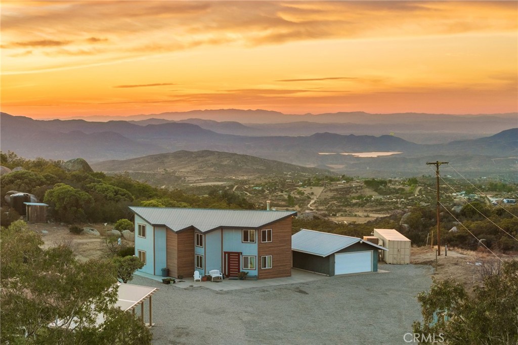Welcome to Windsong Way; A Rare Dual-Home Retreat with Panoramic Views on 8.67 Acres! Discover an extraordinary opportunity to own not one but two turnkey homes nestled in the scenic hillsides of Aguanga. This private, gated-entry property offers breathtaking panoramic views and endless possibilities, all while being just 30 minutes from Temecula or Idyllwild. The main home, built in 1983, spans 1,503 square feet and exudes a modern rustic charm with exposed wooden beams and contemporary lighting. Its open-concept living and dining area features a cozy wood-burning/pellet stove, leading to a remodeled kitchen with granite countertops, stainless steel appliances, a farmhouse sink, and pantry. The first floor includes a spacious bedroom and a remodeled bathroom/laundry room with custom-tiled walk-in shower and dual showerheads with outdoor access. A stunning spiral staircase leads to the second floor, where a versatile loft space and the primary suite await. The primary suite boasts a walk-in closet, a remodeled ensuite with a soaking tub and shower, and access to a large wooden deck (with staircase) with spectacular sunset views over Vail Lake. The second home, built in 2015, is a 1,458-square-foot manufactured home on a permanent foundation. This home features three bedrooms, two bathrooms, a kitchen with granite countertops and a large island, and durable LVP flooring throughout. The primary suite offers a soaking tub and standalone shower, while the home also includes a laundry/mud room. Both homes have their own utilities, including water filtration, propane, and septic systems. Both homes share a well with multiple tanks. Additional property features include a standalone two-car garage or workshop, RV hookups, a shooting range, hiking trails, and storage sheds. Perfect for multi-generational living, rental income, or hosting guests, this unique property allows you to embrace tranquility while remaining a short drive from town. Don’t miss this incredible opportunity—schedule your private tour today!