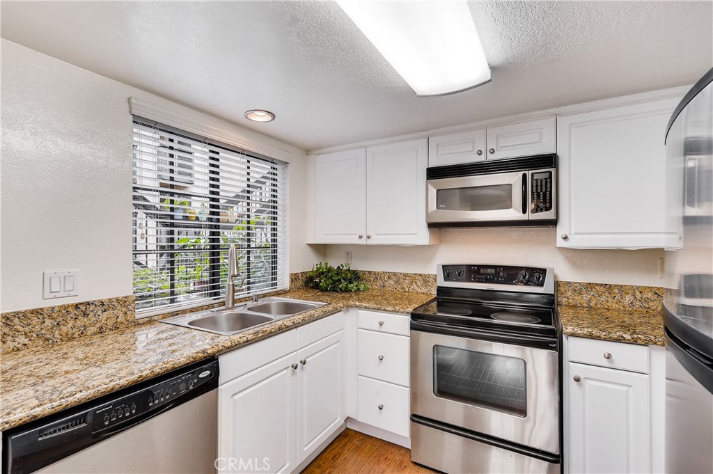 Single level, lower floor, end unit, 1 bedroom condo with large, covered patio in the desirable Bella Tierra community. A beautiful, gated community with mature trees, pool, spa and exercise room. Be the first to enjoy BRAND NEW UPGRADED KITCHEN APPLIANCE PACKAGE. Turnkey. Brand new interior paint. Best priced 1 bedroom condo in Laguna Hills. Attractive wood like floors throughout. Condo has a good-sized living room with fireplace and slider that leads to the covered patio. Dining room is separated from the living room by a half wall for a great open feeling. Cheerful kitchen has white cabinets, granite counter tops and a large window over the kitchen sink. White shaker style cabinet doors with soft close hinges, new drawer boxes, faces and glides will soon be installed for an updated kitchen with brand-new, upgraded stainless-steel appliances, including 3 rack dishwasher, self-cleaning/ steam clean electric range, built in microwave and French door refrigerator with ice maker and filtered water. (These items are not shown in photos.) Bedroom suite vanity has granite counter-top with new high-necked faucet, recessed lights, separate tub/shower and toilet area, and a spacious walk-in closet. Large bedroom with slider that lets in lots of light, leads to the patio. Covered patio also features approximately 5’x 8’ storage room with hook ups for your full-sized washer and gas dryer, gas water heater and room for additional storage. Newer HVAC system and water heater. Condo was re-piped. Assigned carport #17, uncovered spot for second car may be applied for with HOA, plus lots of guest parking. HOA includes water, trash and exterior maintenance. Community pool, spa, gym, club house and shared bicycle storage. No Mello Roos! Dog park and Sheep Hills Park is nearby. Close to the 5 freeway, 73 toll road, Laguna Beach and Dana Point Harbor and beaches.