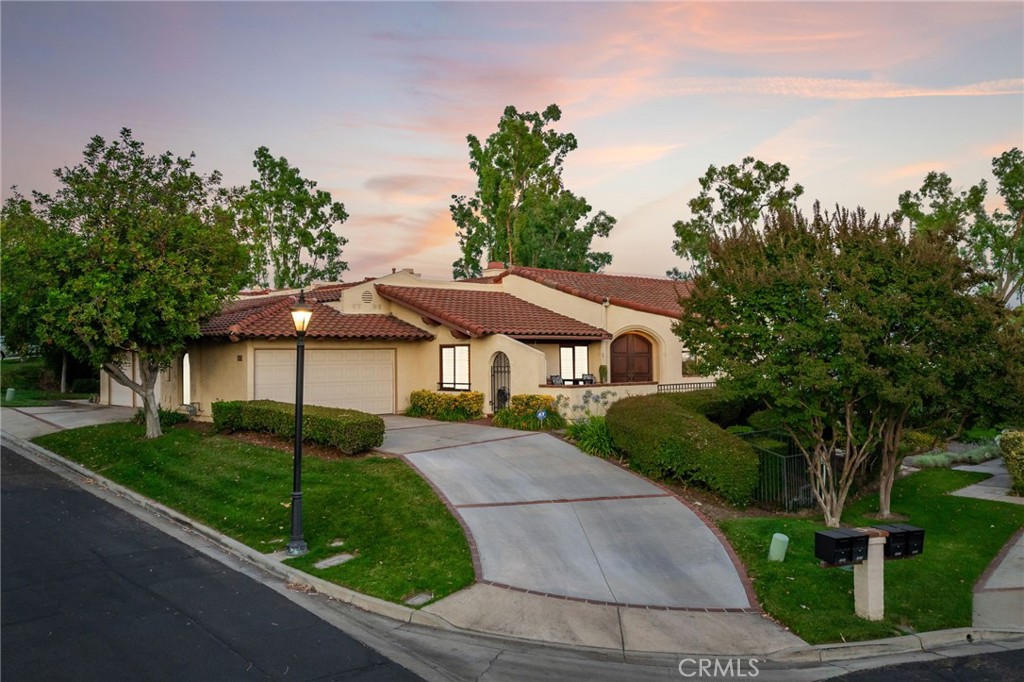 Panoramic View Property on a Prime Corner Lot in Mountain Meadows Terrace Gated Community. Located in the prestigious Mountain Meadows Terrace gated enclave, this elevated corner-lot home showcases stunning panoramic views and impressive curb appeal. A sweeping concrete driveway with brick ribbon inlay leads to manicured landscaping, mature trees, and a gated front courtyard with classic herringbone brick decking. The arched front entry with double doors sets a warm and elegant tone. Inside, rich hardwood floors extend across the open floor plan with soaring vaulted ceilings. Just off the entry, a cozy den or home office enjoys open sightlines into the main living space. The living room features hardwood floors, a charming brick fireplace, and a French door leading to the backyard. Adjacent is a formal dining room wrapped in windows, with French doors on both sides allowing for natural light and seamless outdoor access. The kitchen offers wood cabinetry, granite countertops, stainless steel appliances, recessed lighting, and a peninsula with bar seating. A breakfast nook captures stunning views and provides the perfect place for relaxed dining or morning coffee. On the opposite side of the home, the family room includes a skylight, wet bar, and sliding glass door to a private brick patio fully enclosed by the home’s walls—ideal for quiet evenings or intimate entertaining. The mid-level features a guest bedroom, full bathroom, laundry room, and direct garage access. Upstairs, the primary suite is a private retreat with double entry doors, vaulted ceilings, and a sliding door with plantation shutters that opens to a view balcony. The ensuite bath includes dual sinks, a vanity counter, a soaking tub surrounded by detailed tile work, a walk-in shower with a glass enclosure, and a generous walk-in closet. The backyard offers a full herringbone brick deck, a covered patio, perimeter planters with accent lighting, and a wrought iron and stucco wall that maintains privacy without sacrificing the sweeping view. A side gate provides easy access to the front yard. This thoughtfully designed home blends comfort, style, and location—all in one of Pomona’s most desirable hillside communities.