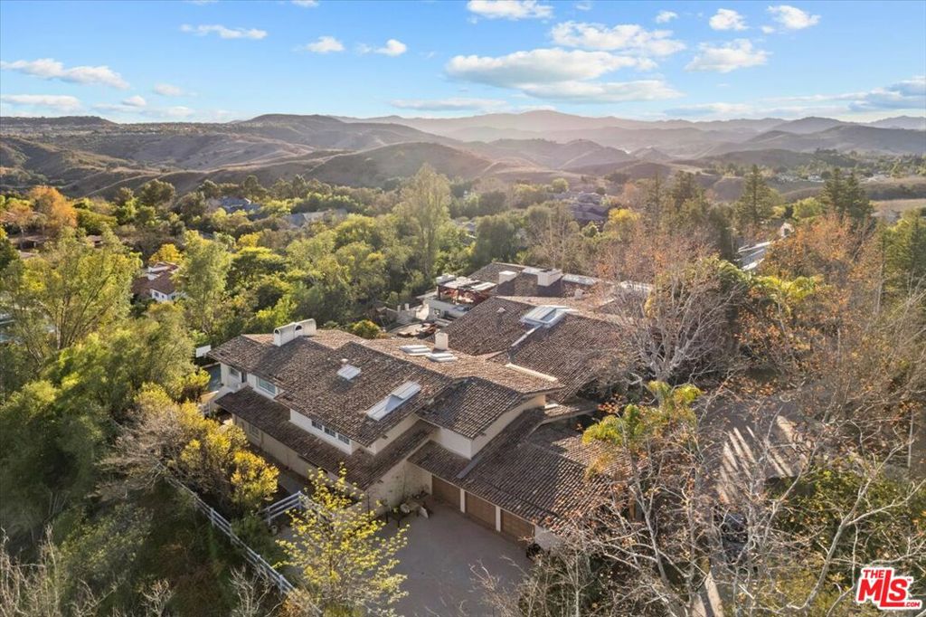 Sited on nearly an acre and a half in the exclusive Ashley Ridge enclave of guard-gated Hidden Hills, this 16,000 SqFt custom designed estate is complete with impeccable details and a backdrop of canyon vistas. A private circular driveway and manicured lawn are canopied in mature trees, welcoming you to the middle of a three-peak architectural build through a grand arched doorway. Bespoke wooden ceilings laid in oak beams contrast the sleek limestone flooring to frame walls of glass, showcasing an irreplaceable view. The craftsmanship of the highest regard detail each room through grand open skylights, perfectly spaced and flushed custom lighting, carved wooden doors, built-in shelving, marble fireplaces, and deep green indoor landscaping with gorgeous mature trees bringing a balance of vibrance and life to the home. The open floor plan draws you through to the picturesque windows lining the rear wall, featuring an artisan bar seating five in length, with a sink, refrigerator, temperature-controlled wine storage, and marble countertops. To your right, the chefs' kitchen and breakfast corner is bathed in natural light from a center peak skylight and brought to life by dark wooden cabinetry and island paneling, matching stone countertops and backslash, and a built-in floating fireplace curated in the same clay as the kitchen hood above the 7-range burner stove. Top-of-the-line stainless steel Viking appliances, dual ovens, a warmer tray, and dual sinks are all built in to create both a luxurious and functional space. The main level is complete with a formal dining room, a lounge with a wet bar and fireplace, an ornate mahogany office/library, and two en-suite bedrooms. Ascend upstairs to the royal primary wing offering gorgeous wooden flooring and beams, a fireplace, a separate lounge room with a kitchenette, a custom double-sized walk-in closet, and a spa-like bath finished in marble flooring, bright windows, an open skylight, a relaxing sitting tub and glass standing shower. Outside, the upper deck is anchored by a sparkling pool and spa, lush foliage, a fire pit and veranda balcony, and a separate covered loggia with a seating area with a TV, fireplace, and a full outdoor kitchenette, cooktop, and Viking grill. Explore down the stairs to a grand flat yard space, a full-sized basketball court, a wooden walkway to the side yard with raised beds for gardening plants and vegetables, and a playground, all overlooking the Santa Susana Mountain Range. The owner worked for over two years closely with the Architectural and Design firm, Iqosa, to develop creative yet meticulous plans totaling 19,000 SF should the new owners like to explore a reimagined project in both architecture and interior decor. The refreshed plans include 9-bedrooms, 2-service quarters, a full theater, gym, spa, and a redesigned chef kitchen all submitted and approved with the city of Hidden Hills and HOA. This sophisticated estate is boasting of exclusivity, design, and quality while being equipped with amenities for both families and an entertainer and sited in one of the safest, most coveted school districts and communities in the country.