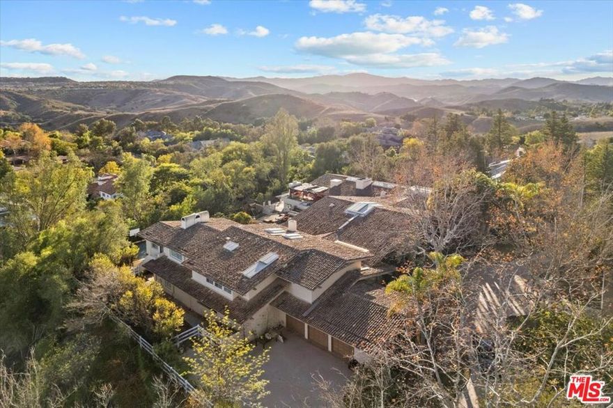 Sited on nearly an acre and a half in the exclusive Ashley Ridge enclave of guard-gated Hidden Hills, this 16,000 SqFt custom designed estate is complete with impeccable details and a backdrop of canyon vistas. A private circular driveway and manicured lawn are canopied in mature trees, welcoming you to the middle of a three-peak architectural build through a grand arched doorway. Bespoke wooden ceilings laid in oak beams contrast the sleek limestone flooring to frame walls of glass, showcasing an irreplaceable view. The craftsmanship of the highest regard detail each room through grand open skylights, perfectly spaced and flushed custom lighting, carved wooden doors, built-in shelving, marble fireplaces, and deep green indoor landscaping with gorgeous mature trees bringing a balance of vibrance and life to the home. The open floor plan draws you through to the picturesque windows lining the rear wall, featuring an artisan bar seating five in length, with a sink, refrigerator, temperature-controlled wine storage, and marble countertops. To your right, the chefs' kitchen and breakfast corner is bathed in natural light from a center peak skylight and brought to life by dark wooden cabinetry and island paneling, matching stone countertops and backslash, and a built-in floating fireplace curated in the same clay as the kitchen hood above the 7-range burner stove. Top-of-the-line stainless steel Viking appliances, dual ovens, a warmer tray, and dual sinks are all built in to create both a luxurious and functional space. The main level is complete with a formal dining room, a lounge with a wet bar and fireplace, an ornate mahogany office/library, and two en-suite bedrooms. Ascend upstairs to the royal primary wing offering gorgeous wooden flooring and beams, a fireplace, a separate lounge room with a kitchenette, a custom double-sized walk-in closet, and a spa-like bath finished in marble flooring, bright windows, an open skylight, a relaxing sitting tub and glass standing shower. Outside, the upper deck is anchored by a sparkling pool and spa, lush foliage, a fire pit and veranda balcony, and a separate covered loggia with a seating area with a TV, fireplace, and a full outdoor kitchenette, cooktop, and Viking grill. Explore down the stairs to a grand flat yard space, a full-sized basketball court, a wooden walkway to the side yard with raised beds for gardening plants and vegetables, and a playground, all overlooking the Santa Susana Mountain Range. The owner worked for over two years closely with the Architectural and Design firm, Iqosa, to develop creative yet meticulous plans totaling 19,000 SF should the new owners like to explore a reimagined project in both architecture and interior decor. The refreshed plans include 9-bedrooms, 2-service quarters, a full theater, gym, spa, and a redesigned chef kitchen all submitted and approved with the city of Hidden Hills and HOA. This sophisticated estate is boasting of exclusivity, design, and quality while being equipped with amenities for both families and an entertainer and sited in one of the safest, most coveted school districts and communities in the country.