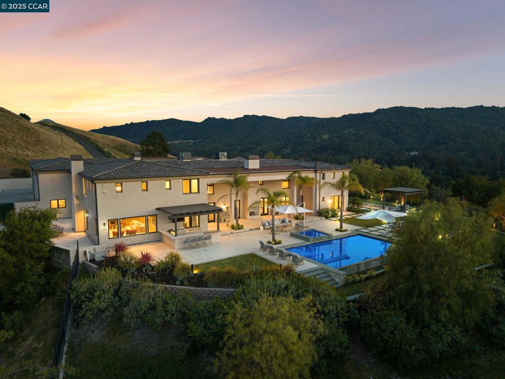 Villa Montecito is more than a home—it’s a private world crafted for those who cherish beauty, seclusion and the art of living exceptionally well. This hilltop 5-acre Santa Barbara-inspired compound offers sweeping panoramic views, masterful design and a lifestyle of effortless luxury, conveniently located mere minutes from downtown Alamo, 30 min. to SF and under an hour to Silicon Valley. A grand entry with fortress-style gates opens to a dramatic courtyard, with lush landscaping and serene water features. At the heart of the home, the great room stuns with exposed beams, double-height ceilings, and cascading chandeliers. Multiple sitting areas flow seamlessly into the dining space, backlit bar, and chef’s kitchen—perfect for both entertaining and intimate living. The primary suite offers a luxurious retreat with a stylish sitting area, spa-like bath, and spacious dual closets. Elsewhere, you'll find an 18-seat movie theater, private office, wine storage, pool table, and media/game rooms. Outdoors, the estate transforms into a resort-style escape with a sleek infinity-edge pool, spa, bocce court, water features and outdoor kitchen. The ADU and office offer additional living and working spaces. A 15-car showroom, workshop, and a 20-car motor court complete this sprawling home.