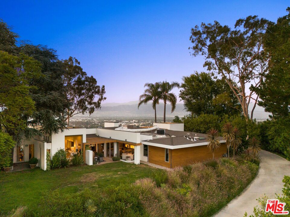 Your own promontory! Inhale, let it out slowly, take a deep breath, you're home. You will feel immediate relief as the gates begin to close, leaving the outside world behind. As you wind up the gentle curves of the driveway you will gaze at the blooming array of trees and foliage. Olive, eucalyptus and citrus line the private drive to your front door. Atop the property resides a single-level modern dwelling shrouded in privacy. As you enter wood accents and concrete floors welcome you into the home. Before you take a tour of this elegantly remodeled home you catch a glimpse of the sweeping views of the San Fernando Valley. You can't help but gasp and say "WOW" that's incredible - as you make your way to a view you have never experienced before."Magical", "stunning", "jaw dropping" - are all words I have heard uttered. Sweeping 180 degree views are simply breathtaking. The city below, the mountains, the planes in the distance, you can see it all, yet it's a world away. Back in the house - floor to ceiling glass windows and aluminum-clad doors frame the open interior spaces allowing the natural surroundings and sunlight into every room. Step-down into a large family room perfect for lounging and enjoy the adjoining outdoor patio with a jasmine covered trellis. The spacious living room with a stone-clad fireplace flowing into the dining area offers an ambience of comfort and the best for entertaining, all while taking in the epic views. The chefs kitchen is spacious and laid out for optimal cooking, complete with a Viking 6-burner dual oven range, Sub-zero refrigerator, warming drawer and pizza oven. You will enjoy the built-in banquette seating area, walls of custom cabinetry and a walk-in pantry. The views while cooking are insane! Slide open the windows and pass the pizza to your outdoor guests! On one side of the house you have the primary suite - graciously sized and a private retreat. Peaceful and calm with views to the outdoor greenery. The primary bath offers a 2-person shower, dual sinks, custom cabinetry and a giant soaking tub with a massive picture window and views to the garden. On the other side of the house you have 3 bedrooms each enjoying its own special view of the outdoors and one full shared bath.The outdoor spaces are magical. The vast grassy lawn encircles the house and is surrounded by an array of greenery. Tall palm trees, mature olive trees and an orchard of fruit trees inc. lemon, grapefruit, apple and avocado. The sparkling & heated swimming pool sitting atop the property creates a resort-like atmosphere. Lounge chairs, a fire pit, umbrellas and outdoor searing embellish your relaxation. An outdoor kitchen with BBQ, sink, fridge, counter space and storage is a great spot for summer dinners. Topping it off is an outdoor shower (where no one can see you!). A "doll house" preciously sitting by itself in the grass, covered in flowering vines, is a welcome abode for the kids to hideaway or for the adults to play. With electricity, windows and finished flooring you will find many uses for this adorable structure. 3-car garage with EV charger and laundry offers a plethora of space for parking and storage. There is a mid-level parking area for gardeners and visitors hence you have ample parking on site. Homes on this stretch of Amanda Drive don't often change hands. A rare opportunity awaits.