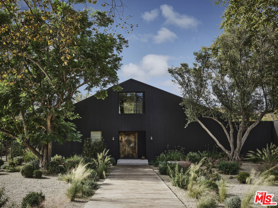 Tucked within the serene Bonsall Canyon - a coveted Malibu enclave renowned for its tree-lined streets and peaceful seclusion just minutes from Point Dumeand Zuma Beach - 6153 Bonsall Drive is a Belgian farmhouse-inspired retreat that seamlessly blends contemporary design with Malibu's laid-back luxury. At once bold and tranquil, this 7,050-square-foot estate rests on 1.3 acres of lush, park-like grounds, offering a lifestyle that celebrates both architectural artistry and the surrounding natural beauty. The vision for this home was brought to life by Vanessa Alexander of Alexander Design, who balanced minimalism and warmth in every detail. Arriving at the home is an experience in itself, with a grand yet grounding processional walkway leading to the striking exterior, clad in custom Shou Sugi Ban wood that lends texture and depth to its barn-like silhouette. Inside, natural light floods the open spaces, illuminating finishes such as imported stone, raw brass accents, and hand-applied plaster walls. Every material feels tactile and intentional, creating an atmosphere of understated sophistication. The heart of the home is an expansive kitchen and family room, where 20-foot vaulted ceilings and seamless indoor-outdoor flow establish a perfect balance of grandeur and livability. The space opens to a sprawling outdoor area, complete with a 60- foot pool, an open-air kitchen, and a dining area designed for unforgettable evenings under Malibu's endless skies. This interplay between interiors and exteriors extends throughout the property, inviting a constant connection to the outdoors. The primary suite takes full advantage of its setting with floor-to-ceiling windows that frame lush views. It is a serene retreat, featuring an oversized walk-in closet and a spa-inspired bathroom outfitted with a soaking tub and a glass-walled marble shower. Thoughtfully designed for both function and indulgence. The home's interiors are curated yet approachable. Custom lighting fixtures, including the sculptural pendant by Rogan Gregory and Pick Up Stick chandelier by Cam Crockford, act as striking focal points, while entertainment spaces such as a game room with a custom pool table and a dedicated movie room add an air of casual elegance. The layout is expansive yet intimate, designed for both grand hosting and quiet evening at home. Outside, the property's grounds offer a private escape. A resort-style pool is surrounded by custom daybeds, an orchard, and a flourishing herb garden, creating a sense of retreat that feels both luxurious and organic. The neighborhood offers seamless access to Malibu's most iconic beaches, scenic hiking trails, and acclaimed dining destinations. Widely featured in Architectural Digest, Elle Decor, Vogue, and The New York Times, 6153 Bonsall Drive is a residence that transcends trends. It embodies the enduring spirit of Malibu: a place where natural beauty, refined design, and soulful living converge. This estate is not just a home; it is an experience, one that leaves an indelible impression with every detail.