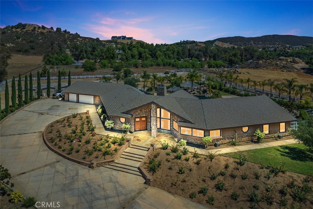Discover the perfect blend of luxury, privacy, and functionality in this single-story estate, nestled in the prestigious La Cresta community. Set on a fully usable, flat parcel accented by natural rock outcroppings, this custom-built home offers designer finishes throughout, 6" exterior insulated walls, and a lifestyle defined by both sophistication and comfort. Step into a grand great room with soaring vaulted ceilings, handcrafted cedar beams, and a dramatic stone fireplace. The expansive, open-concept layout is anchored by a chef’s kitchen, recently upgraded with modern cabinetry, sleek countertops and premium fixtures. Take in panoramic views of the surrounding foothills through the expansive kitchen windows, blending natural beauty with refined living. The thoughtfully designed split-bedroom floor plan includes a luxurious primary suite tucked away for privacy, featuring a spa-inspired en-suite bath and a cedar lined walk-in closet. Secondary bedrooms include a Jack-and-Jill suite and a versatile bonus room with its own fireplace and bath—ideal for a guest retreat, game room, or mother-in-law quarters. All bathrooms throughout the home have been tastefully remodeled with designer selected finishes, elevating both style and comfort. The interior also offers an oversized laundry room with additional storage, utility sink, and central vacuum system. A covered breezeway leads to a 1,200 sq. ft. finished garage deep enough for large trucks or sports cars, complete with a workshop area and utility sink.
Outdoors, your private resort awaits. Enjoy a 50,000 gallon custom pool with beach entry, 10-foot deep end, spa, rock waterfall, waterslide and swim up bar—surrounded by lush landscaping. Gather around the built-in firepit, or entertain under the stars at your outdoor kitchen, featuring a built-in BBQ, spacious prep counters, and a two-burner cooktop. A private well irrigates the entire landscape and outdoor features . Equestrian amenities include two in-and-out corrals with stud panel fencing, large pasture, a tack/feed/storage room, and a riding trail encircling the property. You’ll also find a chicken coop, fruit trees, and raised garden beds, with extra space to expand and bring your outdoor hobbies to life.
The La Cresta lifestyle, where luxury meets freedom and nature. Move-in ready and rich in opportunity, this estate is ready to welcome its next discerning owner.