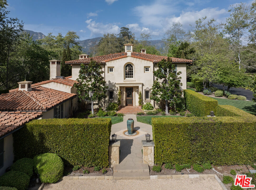 Nestled in the exclusive, gated Montecito Valley Ranch, this luxurious estate is a masterpiece of design by renowned architects Ray Ketzel and Jerry Goodman. Built in 2006, it spans 6,698 square feet on 2.73 acres of flat, usable land, offering both tranquility and modern convenience. The main residence features five spacious bedrooms with en-suite baths, plus two powder rooms. Its open layout seamlessly blends indoor and outdoor spaces, perfect for entertaining. The grand foyer, soaring ceilings with wood beams, and cozy living room with fireplace set the tone for the home. The formal dining room, with custom cabinetry and a butler's pantry, ensures ease for hosting. The chef's kitchen, equipped with top-tier appliances and two islands, opens to the family room, which also boasts a fireplace. Additional flexible spaces include an office, gym, or media room. A main-level bedroom with bath offers a comfortable retreat. The primary suite is an elegant sanctuary with a fireplace, private balcony, and stunning mountain views. Its luxurious bath includes dual vanities, shower, soaking tub, and two custom closets. A 1-bedroom, 2-bath guest house provides extra accommodation. The outdoor area features a pool, spa, outdoor kitchen, and lush landscaping including avocado, citrus, and magnolia trees, plus a raised bed garden for homegrown produce. A 4-car garage, ample guest parking, and proximity to Montecito's best dining, shops, and beaches complete this exceptional estate. Located in the highly regarded Montecito Union School district, this property offers an unmatched living experience.