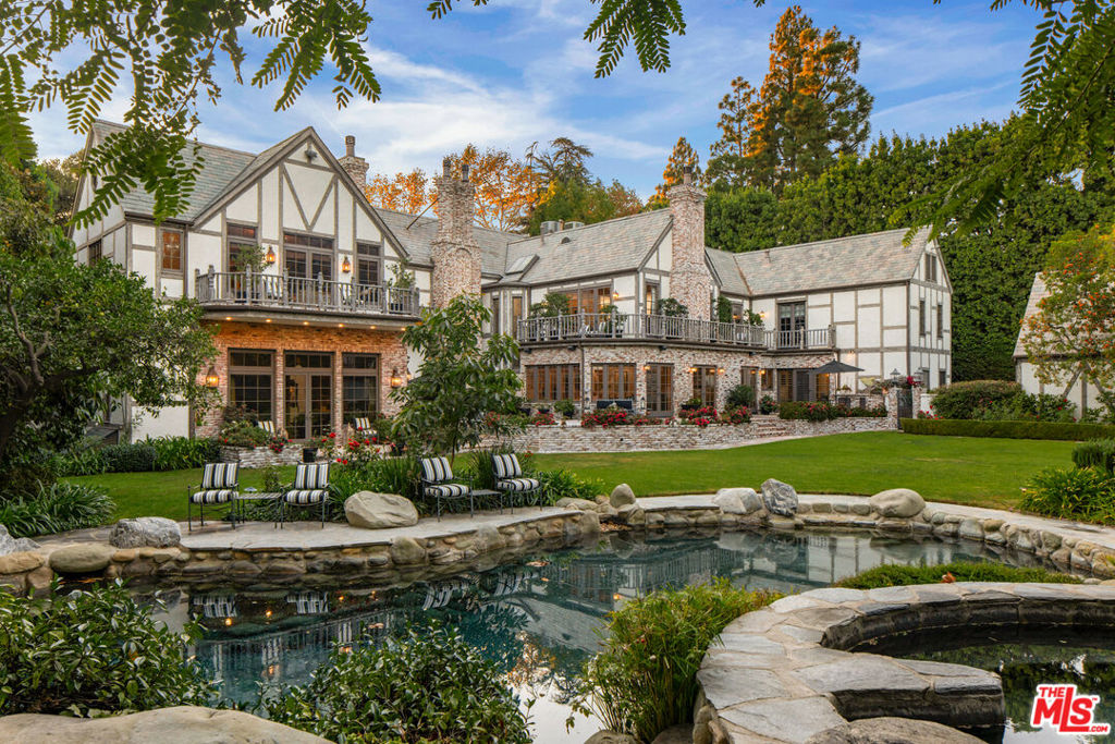 Steeped in Old Hollywood glamour, this extraordinary Beverly Hills estate is more than a home; it's a living piece of cinematic history. Once owned by Harry Warner, co-founder of Warner Bros., this Tudor-style masterpiece has hosted Hollywood royalty, global dignitaries, and some of the most legendary figures of the past century. Adding to its mystique, Marilyn Monroe was rumored to have stayed in the guesthouse, making this estate a true icon of Los Angeles' golden era. Set on a 1.15-acre flat lot with rare street-to-street access, the property offers unparalleled privacy behind three gated entrances. The meticulously landscaped grounds unfold like a private oasis, featuring a north-south championship tennis court, a serene grotto pool and spa, a koi pond framed by lush gardens and romantic fountains, and an expansive lawn perfect for grand entertaining. The charming guesthouse, steeped in its own storied past, houses the a guest suite, offering a private retreat for visitors. Inside, 12,000 square feet of refined luxury blend the romance of Old Hollywood elegance with modern comforts. Exposed rough-hewn beams, intricate hand-carved woodwork, and imported French hardwood floors create an ambiance of warmth and authenticity. The grand arched doorways lead to six opulent bedroom suites in the main residence, alongside an intimate library lounge, billiards room, state-of-the-art screening room, and private fitness center. A professional-grade country kitchen serves as the heart of the home, designed for both intimate family moments and large-scale entertaining. From the cobblestone driveway and porte-cochre to the towering heritage trees and manicured gardens, every detail of this estate reflects unparalleled craftsmanship and prestige. This is not just a residence; it is a rare opportunity to own a true Hollywood legacy, an architectural treasure that continues to captivate and inspire.