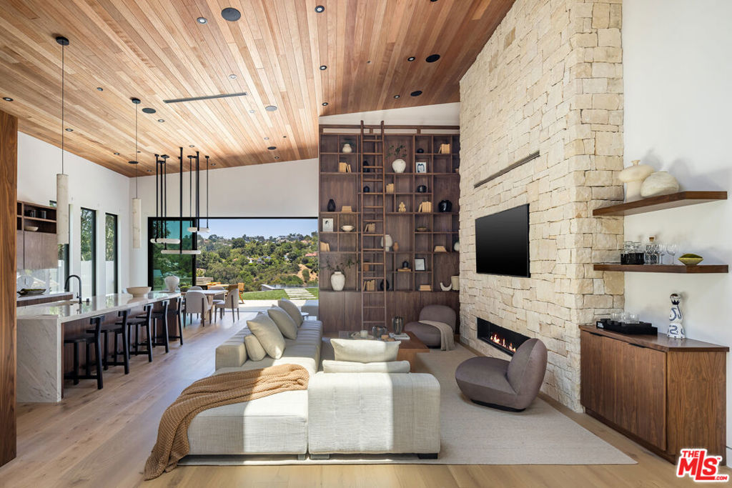 Tucked away on a quiet cul-de-sac in the prestigious Beverly Hills Post Office area, this newly completed modern masterpiece offers breathtaking jetliner canyon views. Privately gated for maximum security and seclusion, the home showcases soaring 18-foot mahogany-clad ceilings, multiple skylights, a dramatic 16-foot-tall library, and expansive sliding glass doors for seamless indoor-outdoor living. The dramatic black-tiled pool, perched on five structural caissons, features a stylish Baja shelf - perfect for lounging in privacy while enjoying the view. Distinctive interior finishes include white oak flooring, Calacatta Cremo countertops in the kitchen, Fantasy Pink marble vanities in the guest suites, and a powder room with Calacatta Picasso marble and Roman clay walls. Custom walnut cabinetry adds warmth and sophistication throughout. The primary suite features a serene sitting area, a large custom walk-in closet, and a spa-like bath with a soaking tub overlooking the stunning views. Outdoors, enjoy a full kitchen equipped with a sink, BBQ, and refrigerator, along with a built-in fire pit perfect for entertaining. Every detail has been thoughtfully curated to elevate both design and function. With world-class finishes and exceptional craftsmanship, this home is a true expression of luxury living.