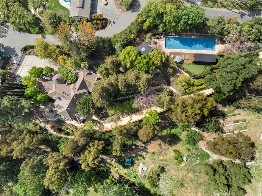 Set across two parcels on over 1.7 acres of lush, magazine-worthy grounds, this custom estate blends refined living with resort-style amenities and natural beauty. The 4-bedroom, 4.5-bath residence is surrounded by mature landscaping, a seasonal river, walking paths, and an impressive variety of fruit trees including Fuji apple, Asian pear, loquat, avocado, peach, dragon fruit, and flourishing grape and passion fruit vines. Inside, wood floors run throughout an open-concept layout filled with natural light. The living room presents a stacked stone fireplace, custom chandelier, soaring ceilings, and tall glass French doors that open to the outdoor space. The dining room features full accordion doors for seamless indoor-outdoor living, while the adjacent office/flex space is complete with built-ins, high ceilings, and French door entry. A showcase kitchen anchors the home, offering quartzite counters, a Wolf range, dual Rohl sinks (including a large prep sink), Sub-Zero built-in refrigerator, Bosch dishwasher, and a walk-in pantry with glass door. An additional drawer-style freezer and separate ice maker add thoughtful luxury. The family room includes a stone fireplace, wine fridge, and direct access to the outdoor lounge. The spacious main level en-suite bedroom is ideal for guests, while upstairs, the primary suite boasts a marble fireplace, viewing balcony, spa-like bath with dual sinks, soaking tub, oversized shower, privacy toilet, and a large walk-in closet. Additional bedrooms share a well-appointed bath with dual sinks, privacy toilet, and oversized shower. A loft-style gym with tile floors and game area below is accessible from both upstairs and the garage. Exterior highlights include a 1/2 Olympic pool, covered lounge, spa, putting green, built-in BBQ, and detached private retreat with dry sauna and shower. A two-car garage, separate road access, and proximity to Bent Tree Park and Peters Canyon complete this one-of-a-kind property.