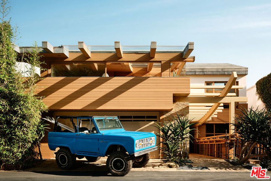 This architectural marvel features an intricate blend of vertical and horizontal planes of wood, stone, and metal, bathed in natural light streaming through sliding glass walls, strategically placed skylights, and an artistic glass floor. Designed by architect Jay Vanos, the finest woodworkers used American Southern cypress for its durability and golden hue on the floors and walls, complemented by a soaring wave redwood ceiling. With ocean views from almost every room, the home boasts a great room with a fireplace, a sitting/dining area, a gourmet kitchen with high-end appliances, and glass walls that open to an outdoor deck perfect for intimate or lavish entertaining. It includes three spacious master suites with fireplaces, luxurious spa-like baths, large closets, and ocean view decks, along with two additional bedrooms. Additional spaces include a sun-filled office/den, a cozy reading/library area, an art studio, an indoor sauna, a zen-style wellness area with sauna and cold plunge, and more. Steps lead to a lower-level surfboard storage area and provide direct access to the beach and renowned Latigo surf spot, making it an ideal home for surfing enthusiasts.