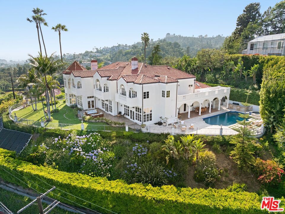 Perched high above Los Feliz, this extraordinary estate, available for the first time in decades, offers breathtaking 270-degree panoramic views from nearly every room. A grand two-story foyer with soaring ceilings sets the tone for the home's elegant yet inviting atmosphere.The expansive dining room and family room showcase the stunning vistas, while the downstairs library/office with its wood-paneled bookcases and sweeping outlooks. The chef's kitchen features a spacious dining area, complemented by a separate prep kitchen perfect for both everyday living and grand entertaining. Upstairs, the primary suite boasts a fireplace, a spacious sitting area with city views, a spa-like bathroom, and multiple walk-in closets. Two additional generously sized bedrooms, each with en-suite bathrooms and private balconies, provide ample space for family or guests. A fourth bedroom and a sprawling media room/gym complete with a grand terrace overlooking the pool round out the upper level. Outside, the resort-style backyard is an entertainer's dream, featuring a solar-heated pool and spa under the stars. This exceptional home must be seen in person to be fully appreciated.