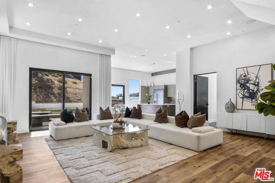 Experience contemporary living in this striking two-level Hollywood Hills home, rebuilt from the ground up in 2013. Set on over a 16,200 sq ft lot, this approx. 3,000 sq ft residence showcases sweeping canyon views, walls of glass, and seamless indoor-outdoor flow. The open-concept layout features soaring ceilings, recessed lighting, and wide-plank hardwood floors throughout. The designer kitchen comes equipped with premium Viking appliances, sleek Silestone countertops, and a spacious island ideal for entertaining. The primary suite offers dual walk-in closets, a spa-inspired bath with jetted tub, and French doors leading to a private wrap-around terrace totaling approx. 1,000 sq ft. Outside, enjoy a heated saltwater pool with waterfall feature, built-in fire pit, and integrated surround sound for the perfect California lifestyle. A rare blend of privacy, modern luxury, and timeless design schedule your private showing today.