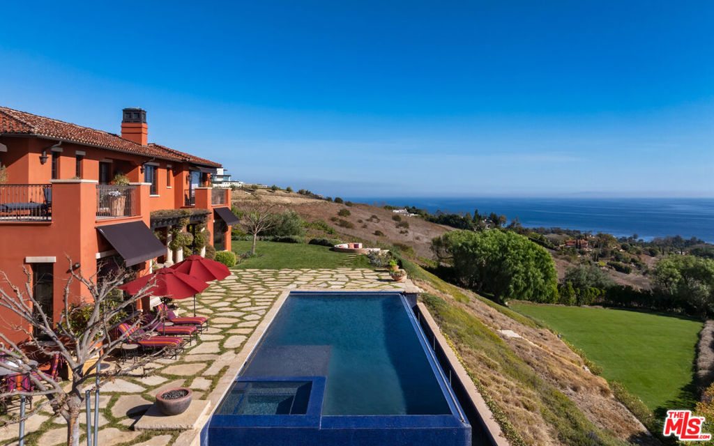 Enter through a grand metal, glass, and wood front door framed by a stone doorway, where breathtaking ocean views immediately greet you. The foyer boasts soaring wood-beamed ceilings and a chandelier, setting the tone for refined elegance. To the right, the formal dining room features high wood-beamed ceilings, arched entryways, and a butler's pantry. Steps lead down to the Main Gallery, lined with barrel ceiling arches and light fixtures.The chef's kitchen is designed for both beauty and functionality, featuring an oversized island with bar seating, stone counters, and wood-beamed ceilings. Premium Wolf appliances, including a double oven stove, additional wall oven, six-burner range, pot filler, and hood fan, complete the space. A Subzero fridge, freezer, and refrigeration drawers provide ample storage. Adjacent, an ocean-view breakfast nook offers stunning pool and coastline vistas.The Family Room includes two sets of French doors opening to the backyard and also features a sliding folding wall system/accordion doors leading to the loggia. An outdoor fireplace and heaters extend the living space year-round. A second living area, accessed through a stone-lined hallway, showcases French limestone floors, an Antilles fireplace, and panoramic ocean views. Behind it, a wet bar with Italian marble countertops with a leather finish, built-ins, and a mini fridge enhances the space.Upstairs, ocean-view bedrooms feature wood floors, large closets, and en-suite baths with stone counters and showers. A guest suite boasts a balcony, high ceilings, and pink marble counters with a shower-over-tub design. The primary suite is an exquisite retreat with a fireplace, a wet bar with a mini fridge, and two expansive closets. The second primary bath features a freestanding jetted tub, a double sink vanity, a shower stall with ocean views, and a private water closet.A stately library off the Main Gallery includes custom built-ins, a cupola, a rolling ladder, and French doors opening to the backyard. An elevator provides convenient access to all three floors. The entertainment level features French limestone floors, a bar with a marble countertop, stone counters, a sink, and a mini fridge. A full gym and a movie theater, which seats 20 comfortably, complete the space.The backyard is a breathtaking sanctuary, with a formal rose garden, an infinity pool with panoramic ocean views, and an outdoor kitchen with a BBQ and bar seating. A built-in couch surrounds a fire pit. Steps lead to a grassy area and an orchard filled with fruit trees. The front yard boasts a lavender garden, privacy hedges, and an expansive carport, while the garage features two 220-volt chargers, alongside space for over 20 vehicles.Additional features include a security system, Tesla power walls, prewired generator capability, electrical closets in the backyard, a doggy door, and a double-enclosed dog run. Crestron automation enhances the home's theater, ensuring a seamless modern experience. Designed by renowned architect Richard Landry, this estate defines coastal luxury, offering an unparalleled blend of sophistication, comfort, and breathtaking natural beauty.