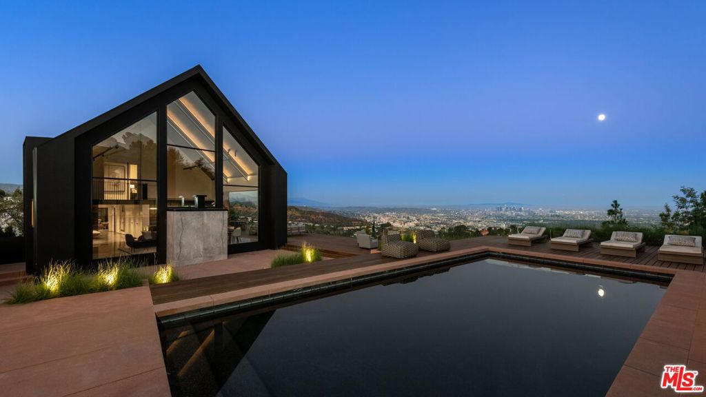 This NOBEL designed modern barnhouse boasting world class architecture and luxury, is a LA gem that's perched atop the infamous Hollywood Hills offers unparalleled 300 degreeviews. All major Los Angeles landmarks are visually attainable from every room of this home. From the city skyline to the famous Hollywood sign, Griffith observatory and a tranquil embrace of the ocean. This meticulously designed sanctuary spans two levels, with 4 bedrooms and 4 bathrooms, this home caters to both privacy and spacious living. Upon entry you'll be greeted by an open floor plan seamlessly integrating the expansive living area with pietra gray marble flooring throughout. The towering windows flood the space with natural light, while Fleetwood doors that collapse into the wall seamlessly blurring the lines between indoor and outdoor living, accentuating the rich textures of pietra marble and wood flooring. The heart of the home boasts two elegant fireplaces, one in the living room and another in the primary bedroom, offering unlimited warmth and ambiance at your disposal. With two primary bedrooms, one on the ground floor and the other on the upper level, feature spacious walk-in closets and luxurious en-suite bathrooms with indulgent tubs and custom vanities. Discover the perfect blend of relaxation and entertainment with a pristine pool deck featuring a pool house which adds the flexibility to use as a private retreat or accommodating guests. The pool house seamlessly flows with the main residence, this entertainer's dream adds an element of sophistication and leisure. Positioned to the south, this home basks in an abundance of natural light, with the breathtaking sun rising in the morning and casting its warm glow over the pool, ensuring you'll enjoy the natural light glistening over the water throughout the day. Completing this extraordinary residence is a three-car garage with a guard room for added security, a long private driveway that climbs nearly 30 feet above street level, and a host of amenities. This home reflects the fusion of art and architecture, capturing the essence of modern luxury with each detail carefully curated to create not just a home, but a living, breathing piece of artistry.