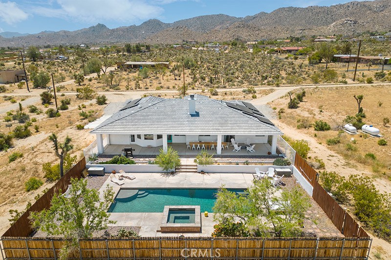 Welcome to resort style living at this gorgeous furnished mezmerizing pool home! Less than 10 minutes from the JTNP, blocks from the village, and surrounded by accessible hiking trails, this stunning modern Mediterranean home has everything you could desire. 4 bedrooms, high ceilings, an open floor plan, updated interior and perfect backyard pool oasis await you on over an acre of land. Walk thru the entry and feel inspired in this bright and stylish single level home. The family room impresses with a wood burning fireplace and open concept kitchen with a peninsula, full suite of built in stainless steel appliances, granite countertops, and an eating nook overlooking the backyard. There are two primary en suites, one featuring a massive jetted tub, separate shower, double sinks, and a walk-in closet! The home also boasts 2 more bedrooms and a full bathroom in addition to a formal dining room (currently in use as a 5th bedroom), pantry, and laundry room. The massive attached garage is easily accessed from inside of the home to make bringing in your groceries a breeze. This home was repainted inside and out including cabinets, has updated appliances and flooring (no more carpet), new electric water heater, PLUS features an owned solar system to keep your electric bill low.
Drop your bags and head straight to the generous backyard where you can sit on the large covered patio with a glass of wine, roast marshmallows on the firepit, experience a soothing sound bath by one of Joshua Tree's many healers and musicians, or serve a fantastic meal. Watch the kids play in the oversized heated in-ground pool until bedtime when you sneak out for a dip in the spa. Beautifully landscaped and fully fenced, you'll only want to leave this oasis to tinker in your giant garage with plenty of space for a workshop or storing your desert toys.
Close to hiking trails and other landmarks like the Joshua Tree National Park, Integratron, Pappy & Harriet's, Pioneertown, JTRC, and popular off roading areas. It is already a highly successful, 5-star short term rental and is perfect for your primary residence, second home, or investment property! Come enjoy your stunning pool and spa in your backyard oasis today.