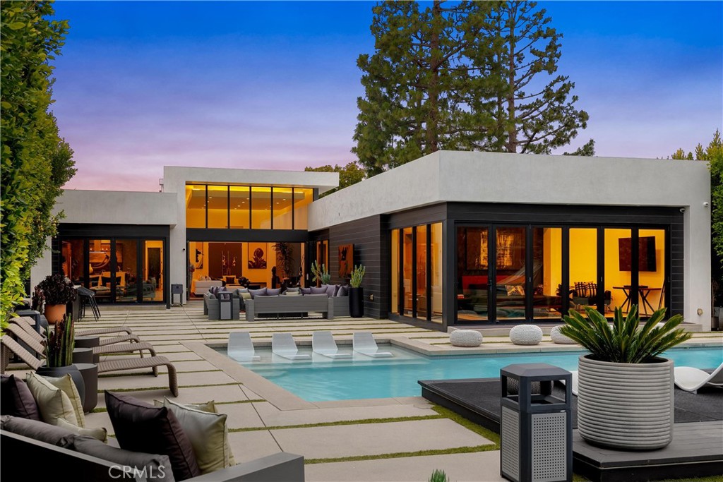 Breathtaking Modern Oasis in the Hollywood Hills. This exceptional 4-bedroom, 5-bathroom contemporary residence sits perched in the prestigious Hollywood Hills, offering unparalleled views of the Griffith Observatory, iconic Hollywood Sign, and San Fernando Valley. The sophisticated one-story design showcases clean architectural lines with a perfect balance of white stucco and dark accent walls.
Step inside to discover an airy, open concept living space. Floor-to-ceiling glass walls flood the interior with natural light while framing the spectacular views. The elegant living room features a comfortable, light-colored sectional, perfect for entertaining or relaxing while taking in the scenery.
The gourmet kitchen boasts sleek cabinetry, premium appliances, and a stylish island with bar seating that opens to the main living areas. The carefully curated neutral palette throughout the home creates a calm, sophisticated atmosphere.
Multiple sliding glass doors blur the boundary between indoors and out, leading to an entertainer's paradise with several distinct outdoor living spaces. The expansive concrete paver patio surrounds a striking swimming pool with in-water loungers. Multiple seating areas, including a cozy fire feature, provide perfect spots to enjoy the breathtaking sunsets and night views. The thoughtfully designed landscape showcases drought-tolerant plantings, mature trees, and architectural succulents that complement the home's modern aesthetic while requiring minimal maintenance. Additional features include a detached studio, epoxy-finished garage floor, and meticulously maintained grounds that create a private sanctuary in one of Los Angeles' most coveted neighborhoods.