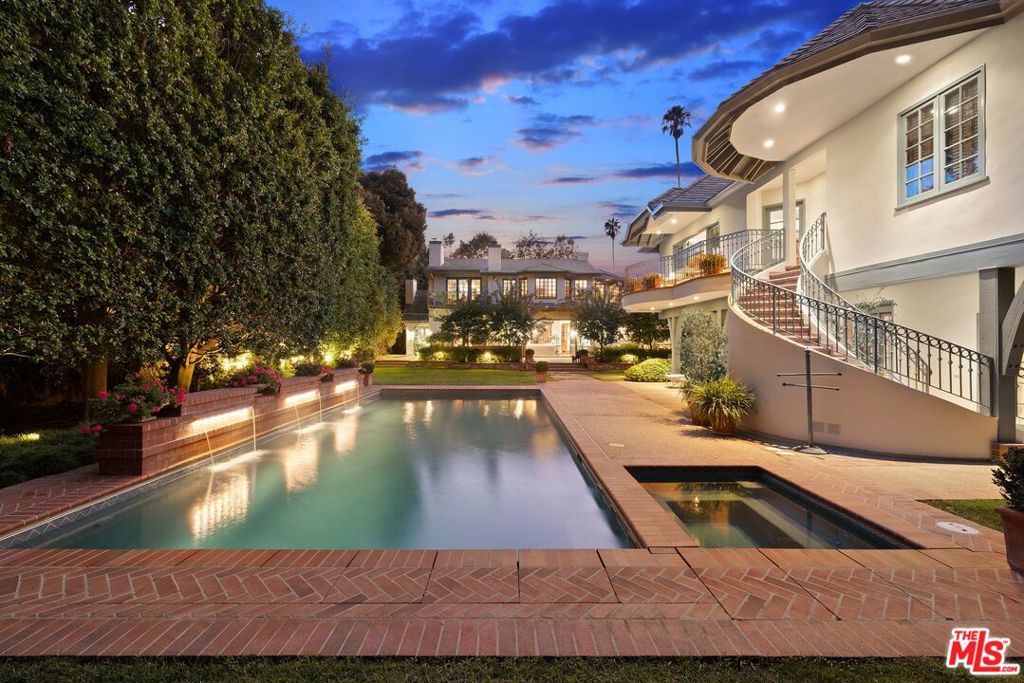 Tucked away behind privacy gates beneath towering, leafy trees in prime Brentwood, this Country French estate promises a serene lifestyle of comfort and elegance set on over half an acre. A lengthy brick-lined driveway leads through a sprawling grassy lawn and into the expansive motor court, complete with parking for numerous vehicles in an enchanting courtyard-like setting. Inside, guests are greeted by a spiral staircase and beautiful chandelier in the foyer. Soft whites and natural woods give the light-filled living room its inviting appeal, highlighted by exposed beams, paned windows, classic mantel, and French doors. The adjacent library with fireplace and built-in shelving is the perfect place for work, study, or quiet reading. A newly updated gourmand's country kitchen is appointed with top-of-the-line appliances including three Gaggenau ovens, Sub-Zero refrigerator, and Miele dishwasher. There is also a butler's pantry with walk-in storeroom and adjacent breakfast area which comfortably seats eight. The formal dining room, with walk-in temperature-controlled wine room, includes a custom buffet and is ideal for dinner parties and family gatherings. In the family room, discover a versatile 210-inch Crestron-controlled Planar LED system, folding glass doors to the outside, coffered ceilings, and wet bar with wine refrigerator and ice maker. Upstairs, the lavish primary suite offers a sitting room with fireplace and private balcony access, dual walk-in closets, linen closet, and a spa-inspired bathroom with two separate vanities and toilet rooms, double shower, and jetted tub. The upgraded and expanded pool house serves as a luxurious guest retreat with a living room, bedroom, gym, bathroom, and sizable office/screening room with a large TV and private balcony overlooking the peaceful rear grounds. The reimagined, resort-style backyard is an entertainer's dream, complete with outdoor kitchen, living, and dining rooms, a grassy yard, a shimmering pool with waterfalls, separate spa, and dog run. Additional home features include updated state-of-the-art security systems, walk-in attic space, and three-car garage with built-ins and storage closet. Enjoy close proximity to Brentwood's world-class dining and eateries, shopping, hiking trails, country clubs, freeways, and important cultural landmarks plus all the Westside offers. Welcome!
