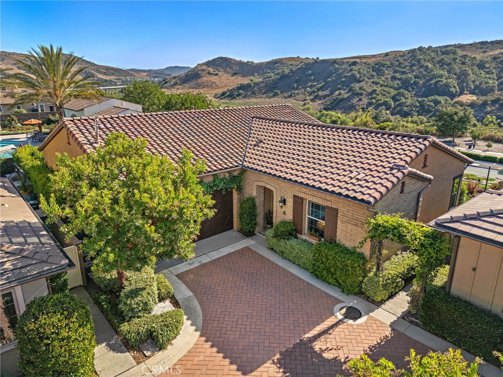 Welcome to this exceptional former model home, perfectly positioned on a private corner lot with panoramic canyon views in the coveted 55+ enclave of Avocet and just steps from the luxurious Outlook Resort Pool. Designed for elevated living, this residence blends refined elegance with thoughtful functionality inside and out. Step inside to discover custom tongue-and-groove ceilings with rich wood beams, setting the tone for the home’s warm and sophisticated aesthetic. The open-concept floor plan features a striking built-in media wall with generous storage, Hunter Douglas motorized shades, and a stylish dining area complete with custom buffet cabinetry and dual wine refrigerators- ideal for entertaining. The chef’s kitchen impresses with upgraded KitchenAid stainless steel appliances, a built-in refrigerator, granite countertops, and a full wall of pantry cabinets with convenient roll-out shelving. Wake up to breathtaking canyon views from the serene primary suite, highlighted by a custom wood accent wall. The spa-inspired ensuite bath offers granite countertops, an oversized soaking tub, a frameless glass shower, and a walk-in closet with premium custom shelving. Two additional bedrooms provide flexible options for guests and the built-in shelving make the perfect space for a home office. Step outside through oversized sliders to your private backyard retreat, featuring a covered outdoor room, built-in fire pit, lush gardens with mature landscaping, and a manicured turf lawn—perfect for entertaining or relaxing beneath the stars. This home also includes owned solar panels and a whole-house water softener system, blending sustainable living with luxury. As part of the award-winning Rancho Mission Viejo community, enjoy access to a multitude of resort-style amenities: 10 pools, 4 fitness centers, clubhouses and scenic parks and trails. Experience the perfect blend of modern comfort, timeless style, and vibrant community living—resort life awaits!