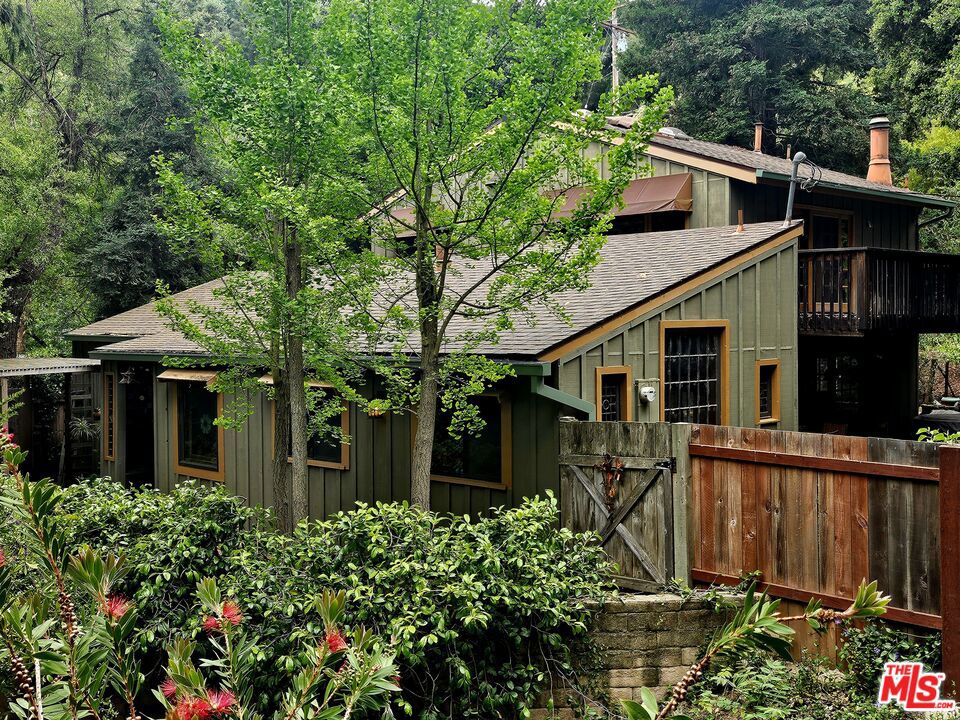 This vintage Topanga creekside family home with mutiple outbuildings is on the market for the first time in 42 years! Step back in time as you cross over the creek on your private footbridge into this fabulous Liberty Lane sanctuary. You'll enter through a beautiful stained glass covered porch into a warm and inviting space with Vermont Castings wood burning stove and built-in sitting area. This brings you to the the true heart of the home, a kitchen with a soaring ceiling and rough hewn red cedar cabinetry with magnificent multi pane and leaded glass windows. Also on this level is a proper dining room, den, 1st floor bedroom and living room with river rock fireplace-- all over-looking a mostly flat yard, graced by a sacred Grandmother Oak with wrap around entertaining deck, Redwoods and multiple fruits trees. The 3 outbuildings provide plenty of storage and options for re-imagining to support all of your creative endeavors. Multiple patios, decks and outdoor living spaces, all within earshot of the seasonal creek, make this entertainer's dream property the ideal backdrop for all of your Topanga Stories...