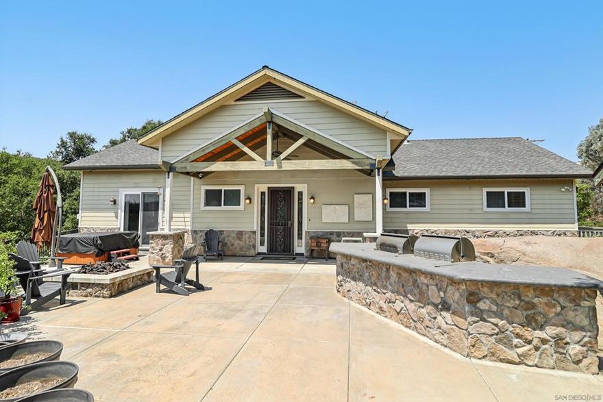 Welcome to Seven Meadows in beautiful Ramona.   Surround yourself in the beauty of nature with majestic oak trees, a seasonal stream, and serene mountain views.    As you enter this retreat-like residence, you are greeted by 2 vineyards, a fruit orchard and a bridge over the stream, leading up to the two residences.    The main home is 3BR/2BA and lives like a single level luxury cabin.   Vaulted beamed ceilings, wood floors, stone accents and a floor to ceiling stone fireplace.   The kitchen blends with knotty pine cabinetry, stainless steel appliances and two breakfast bars with seating for 8, plus a walk-in pantry.   The primary bedroom suite is located on the opposite site and features a sliding glass door to the patio with built in BBQ, pizza oven,  firepit and portable spa.   There are two walk in closets and a luxurious bathroom.   The other wing of the home offers two bedrooms, each with access to a view deck, and sharing a beautifully appointed bathroom.   There is also a full size laundry with plenty of storage!   Downstairs is the attached 1BR/1BA apartment, 2-car garage and RV garage.   RV garage is approx.. 23x17 with a 13x16 room behind including half bath and 220 power.    The 11+ acres whisk you into a lifestyle filled with nature.   With over 50 oak trees, natural rock outcroppings, you will be greeting daily by wildlife including deer.  There are 3 vineyards. The previous owner was a wine maker and yielded over 3000 lbs of grapes between the different varieties:    Zinfandel, Tempranillo, Syrah, Grenache and Mourvedre.  See Supplement  Vines are watered by a well.     Approx. 500 Vines total.  The property is also ideal for multi generational living, or perfect for an investment.  There is one additional home that includes two units.   A 3BR/2BA on the top floor, and a 2BR/2BA on the bottom floor.    Approx. 2900 SF between the two units, plus a garage.   Rental income is currently over $5000/mo for the two units.  Tenants are on a month to month.   There is just one water meter between all the homes, however, Ramona Water District can add a second meter, for a fee of approx.. $25k.    There is plenty of room for horses, livestock and more.   Behind the main residence are two additional cleared sites that could be ideal for animals, workshop etc.   In addition, there is a RV pad with full hook ups that was previously rented for $1500/mo.    Chicken coop, several sheds, rustic accents, lush lawn,  approx.. 125 fruit trees completed this perfect retreat.   Located on the west end of Ramona for easy commute and close to Dos Picos park for hiking and camping.    Seller is in the process of completing another airBnB unit in the oak trees.   1BR with view deck and bathroom, approx.. 120 Sf.