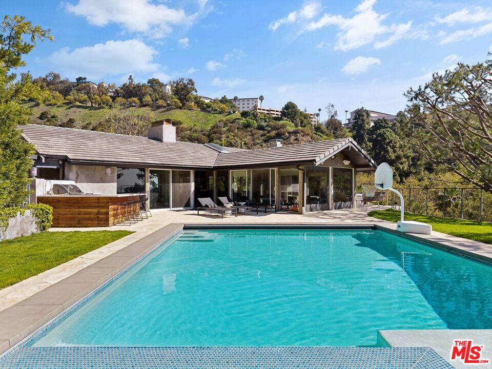 Tucked away just four minutes above Sunset Boulevard, this contemporary estate is perfectly positioned on a serene, low-traffic stretch of North Bundy Drive, offering an exceptional blend of privacy, convenience, and prestige in one of Los Angeles' most sought-after neighborhoods. Situated on an expansive 44,850 sq ft lot, the home offers approx. 6,000 sq ft of living space with 6 bedrooms and 7 full bathrooms. Renovated in 2012, it features an open-concept layout, stylish finishes, and modern upgrades throughout. The chef's kitchen includes quartz countertops, custom cabinetry, premium appliances, and a large center island, with an adjacent dining area showcasing lush hillside views through oversized windows. Light-filled living areas feature contemporary fireplaces, seamless indoor-outdoor flow, and a smart audio system powered by Amazon Alexa. An indoor bar with custom shelving sets the stage for effortless entertaining, while the backyard retreat offers an oversized pool, cabana lounge, full outdoor kitchen with BBQ, and a professionally designed putting green. Additional highlights include a home theater with tiered seating (convertible to a guest suite with full bath), a gym/office setup, solar energy system, EV charging station, natural gas generator, water filtration system, and a spacious basement ideal for storage, recreation, or customization. A rare opportunity for luxury, tranquility, and prime Brentwood living.
