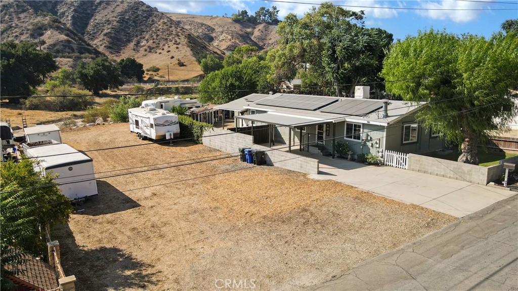 An updated and upgraded home with a extra wide residential lot awaits you. The front carport doubles as a patio and offers covered access to the front door. There is plenty of room for RV's, trucks and equipment on the lot. The home offers a totally remodeled (From the studs out) kitchen and dual pane windows throughout the house. The dining room has built in cabinetry with great storage space. The primary suite has its own bath with a shower stall and separate large soaking tub. The primary bedroom windows offer a view down the canyon to the south. There is an indoor laundry room with its own outside access. The living room offers a free standing wood burning fireplace. Security cameras provide peace of mind across the entire lot. The attached 2 car garage has a built in work bench and there is a cozy office inside the garage with its own AC. At the rear is a fenced yard with chickencoops and a rear exit to the flat area behind the property that is an unused street easement. There are RV hookups at the lot rear that include water and electric access as well as waste disposal. Beyond that is a dry creek bed. The property is only 10 minutes from Valencia shopping, commercial, and medical service centers. The south side of the property has 2 separate vacant lots that could possibly be developed. The buyers should investigate all potential uses. Buyers are advised that the now closed Chiquita Canyon Landfill is within a mile of the subject property to the southeast. It was closed December 31, 2024.